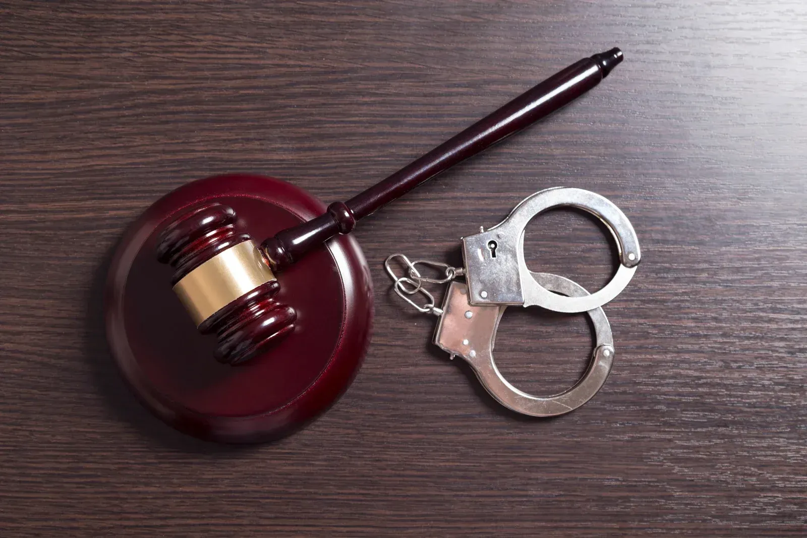 A judge 's gavel and handcuffs are on a wooden table.