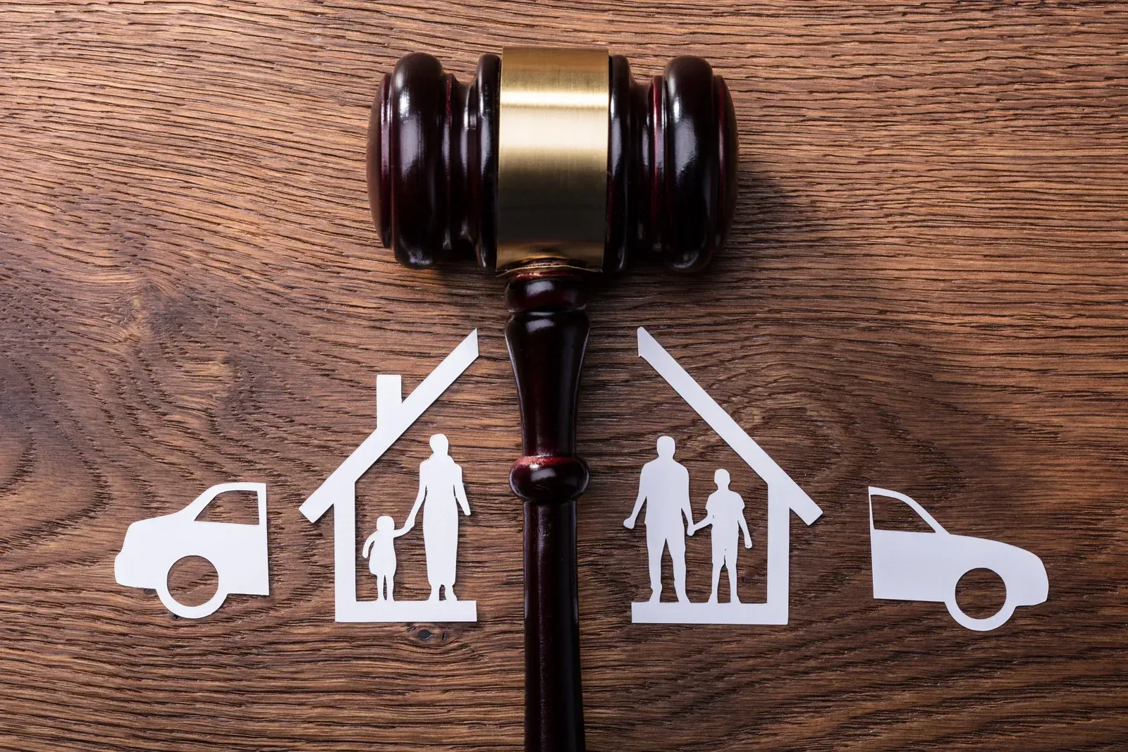 Gavel over paper cutouts of split family homes, cars, symbolizing divorce and property division.