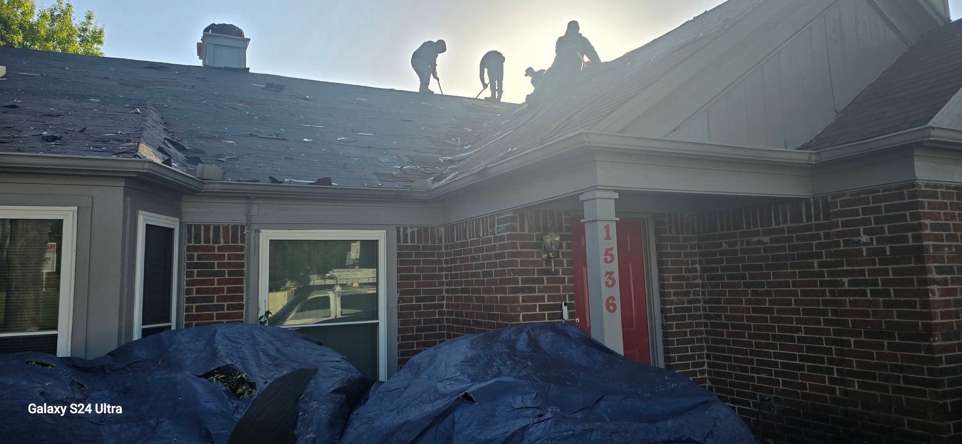People working on a house roof on a sunny day. Tarps cover items on the ground.