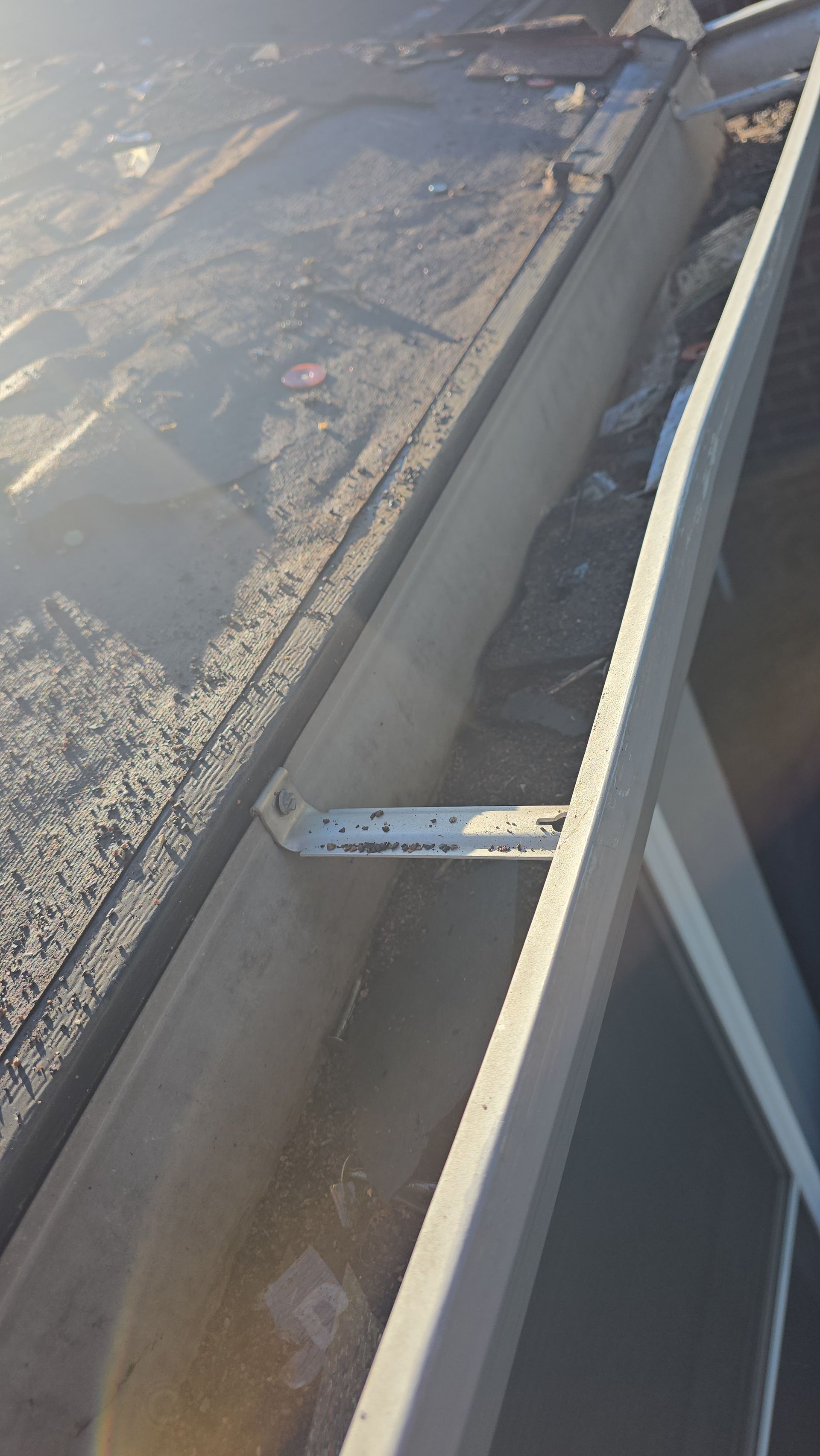 A concrete rain gutter with debris and a metal bracket, seen from an elevated perspective on a sunny day.
