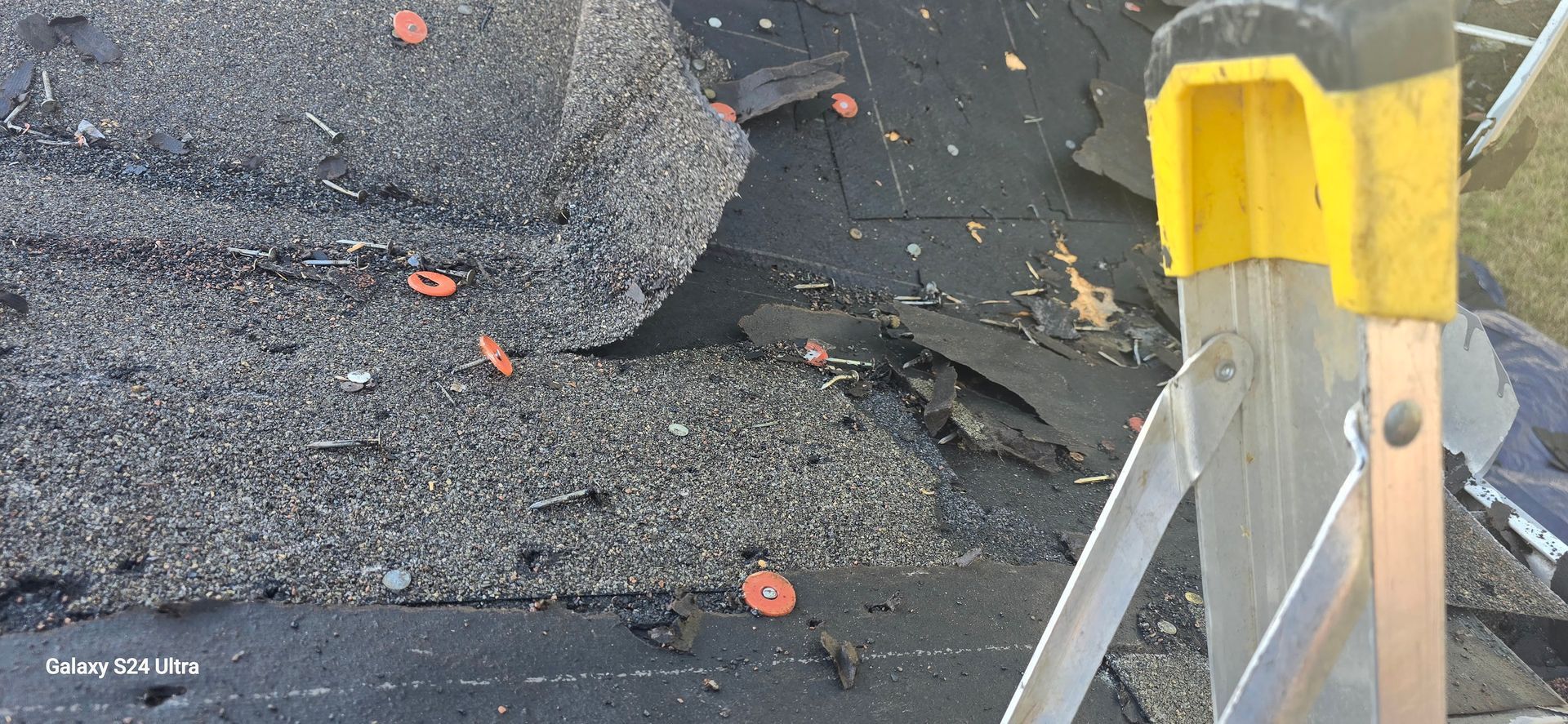 Damaged asphalt shingles on a roof with orange fasteners and a yellow-capped ladder.
