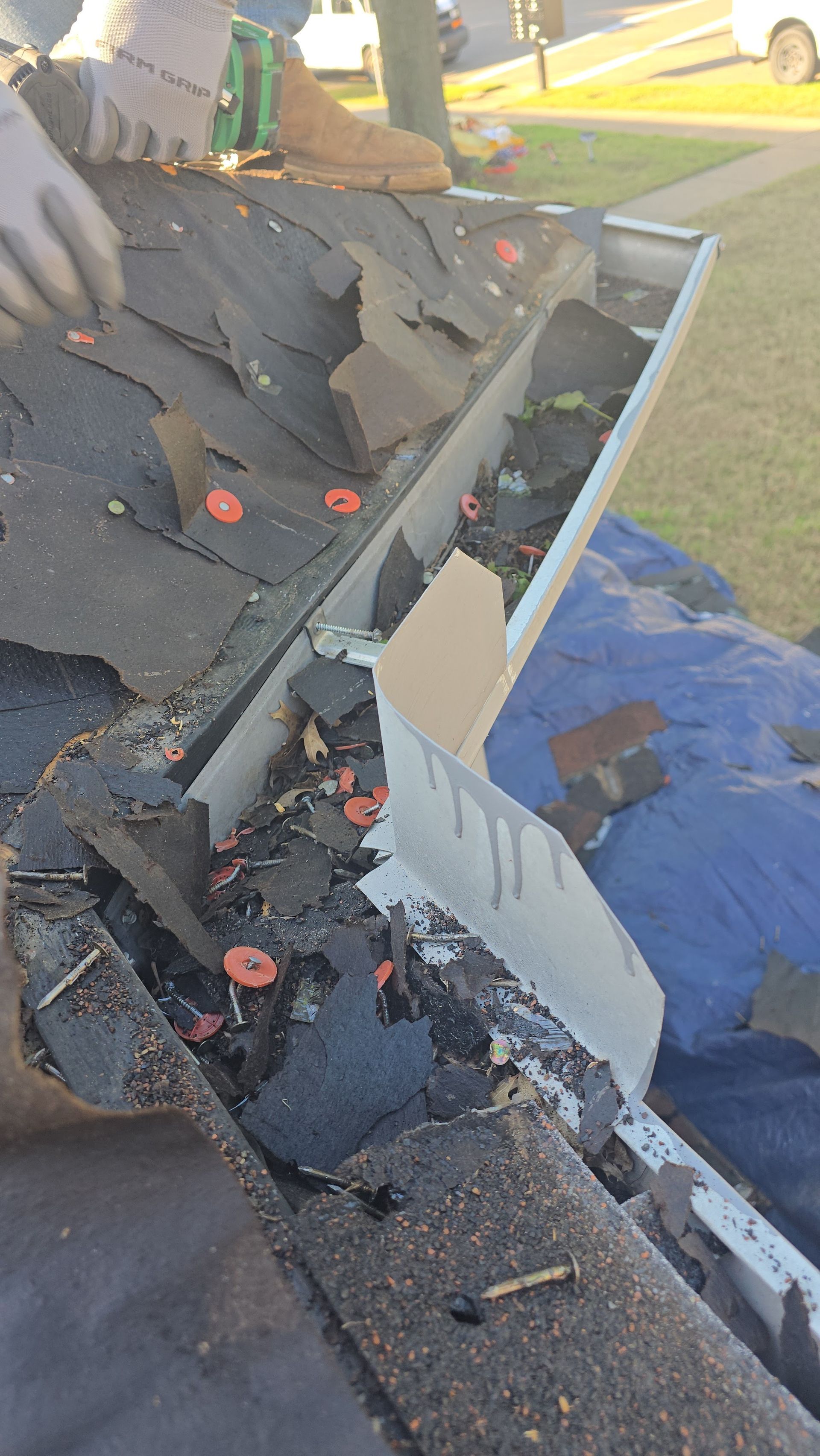 Roofer repairing damaged shingles and gutter on a rooftop, debris visible, orange caps, hands in gloves.