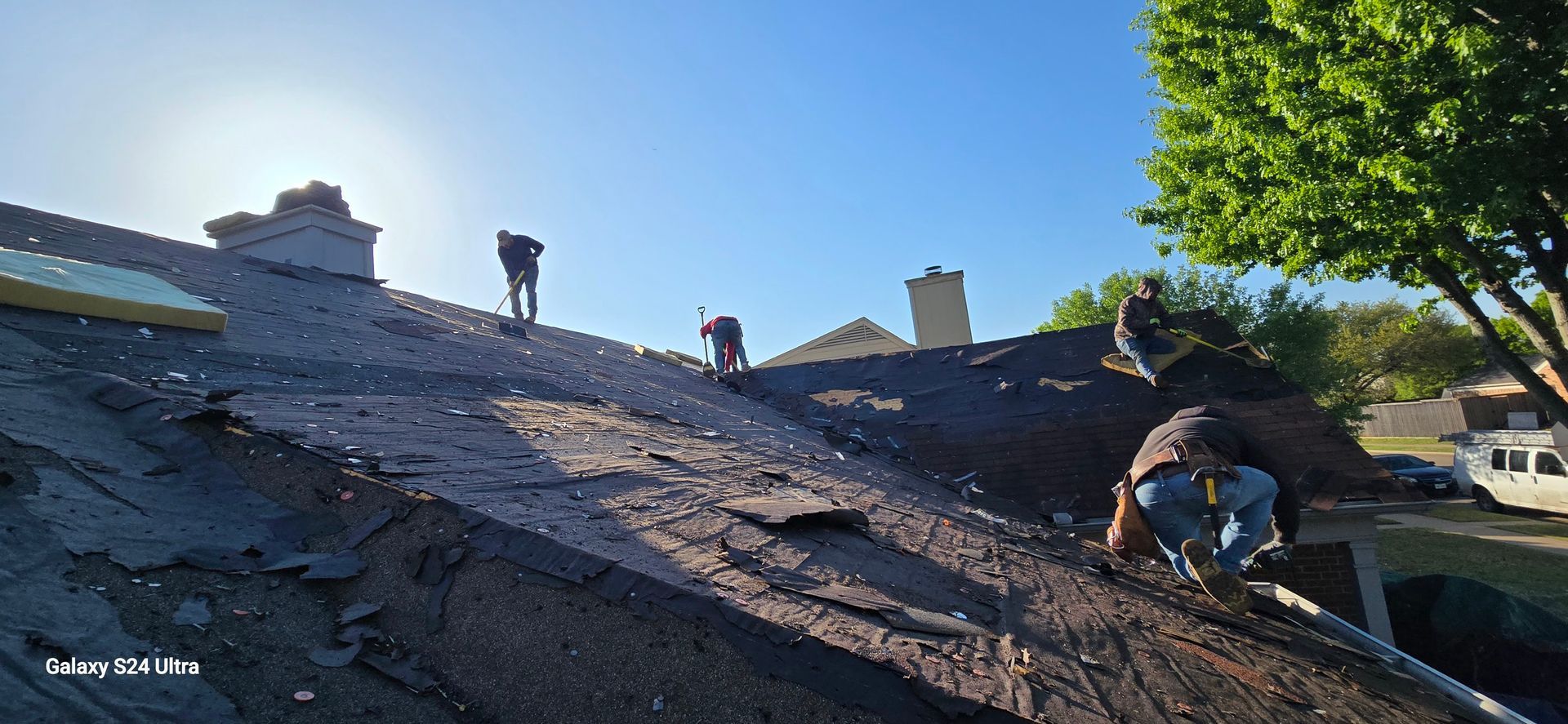 Roofing crew working on a roof under a bright sky.