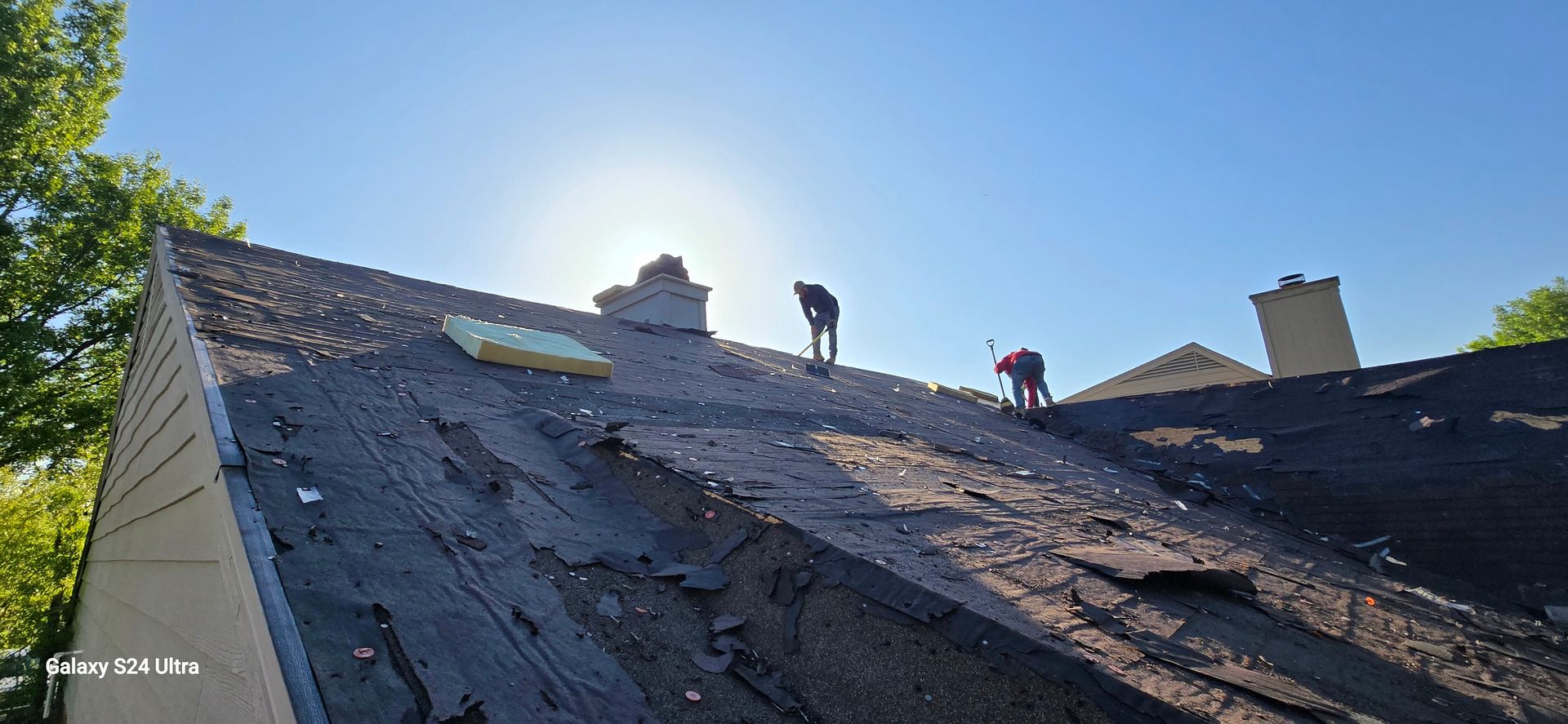 Two people working on a roof under a bright blue sky.