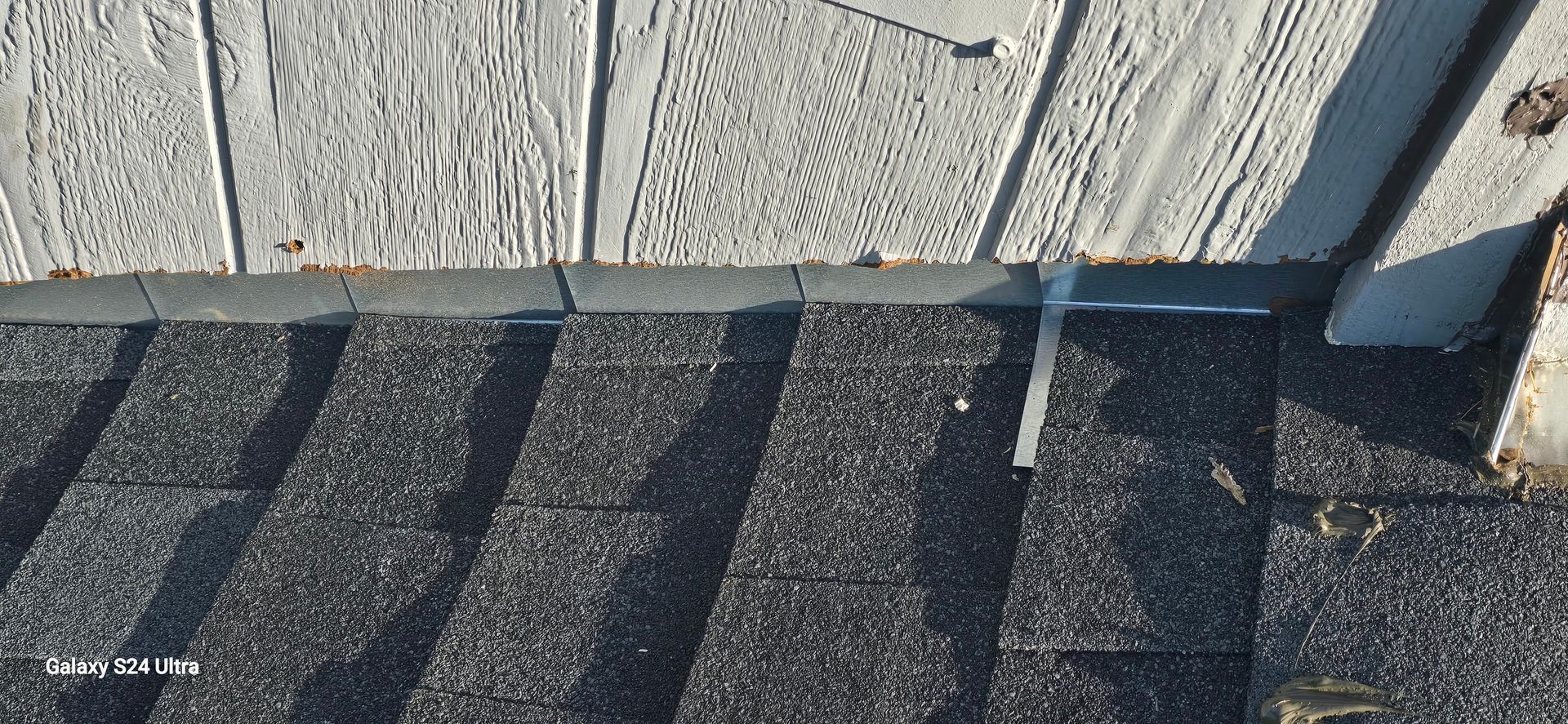 Close-up of a roof edge with shingles, siding, and metal flashing.