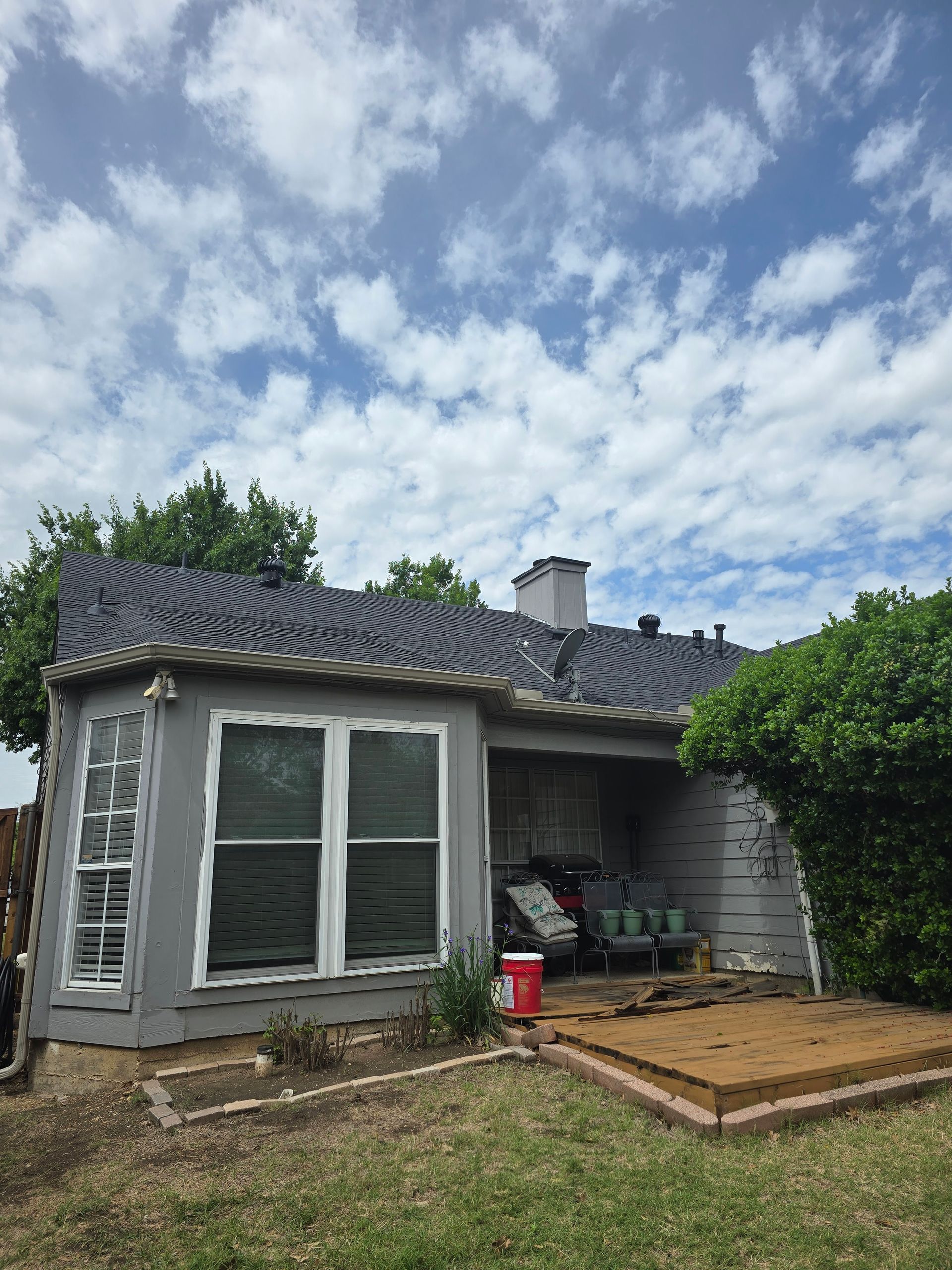 Gray house with a dark roof, windows, and small porch under a blue sky with clouds.