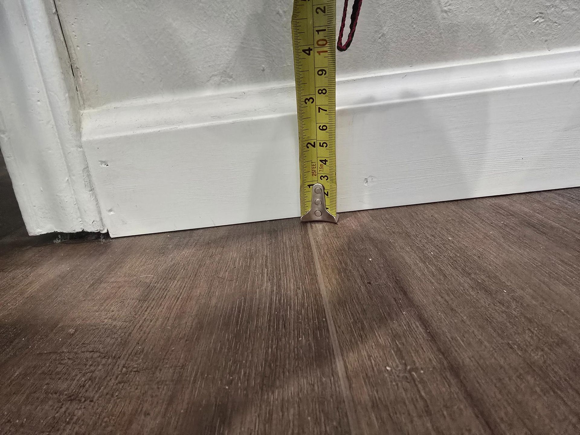 Tape measure on a wood floor, measuring a white baseboard.