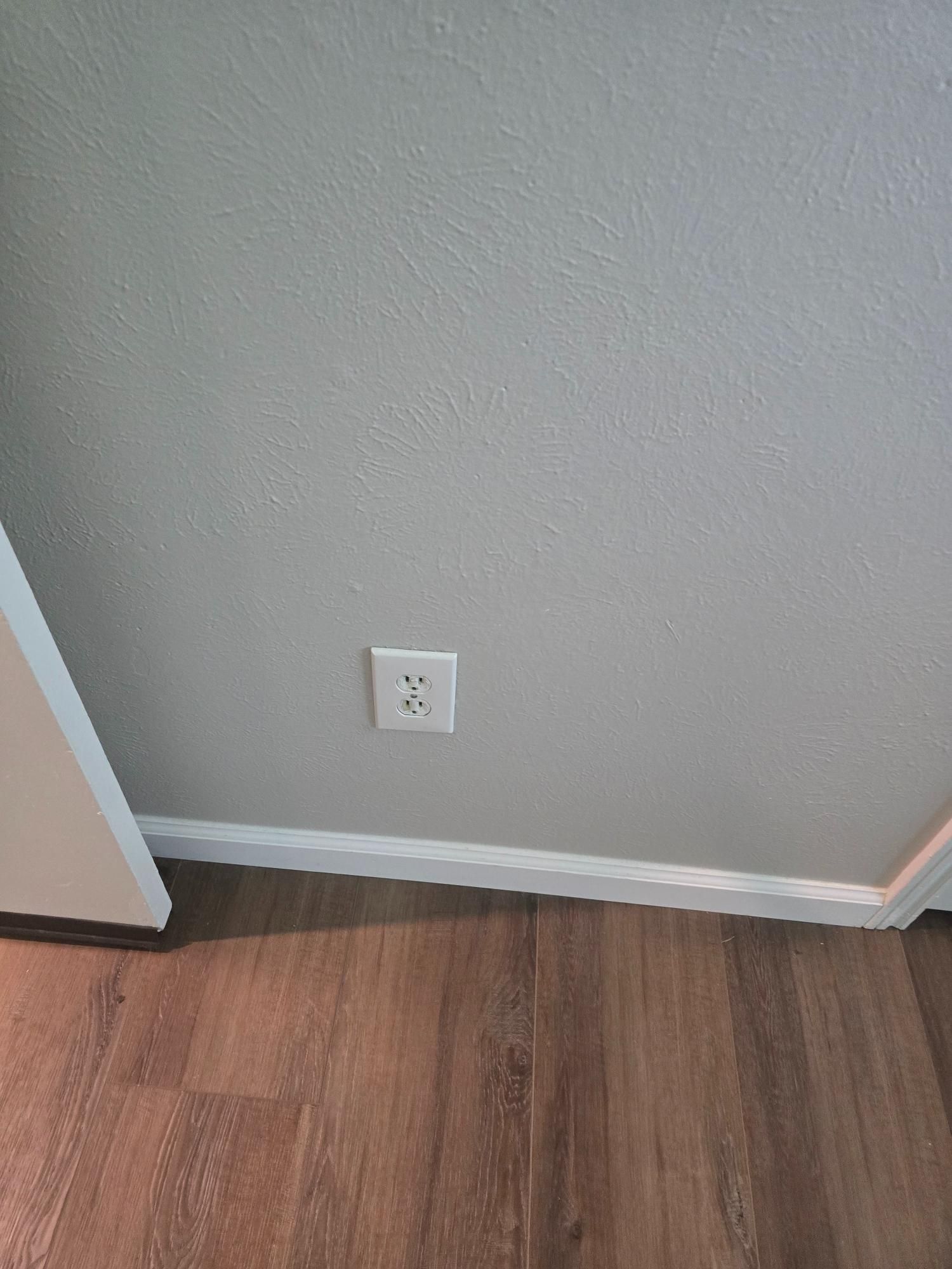 White electrical outlet on a gray wall above wooden flooring.
