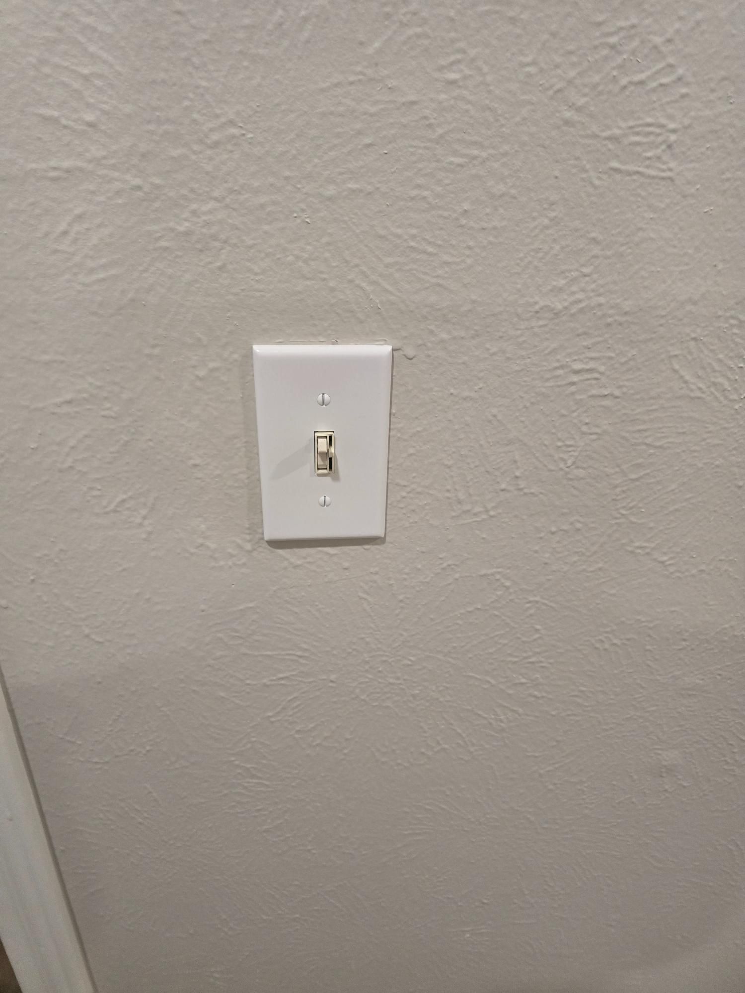 White light switch on textured, off-white wall.