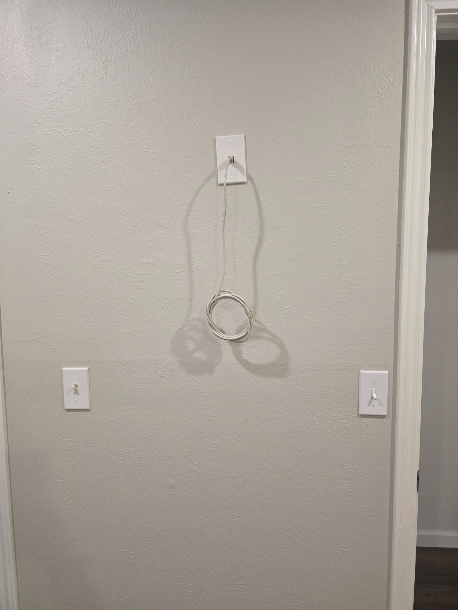 White wall with a wire and cable, two light switches, and a door frame.