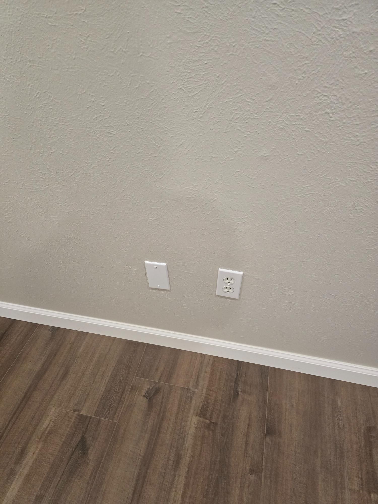 Off-white wall with two electrical outlets above brown wood floor.