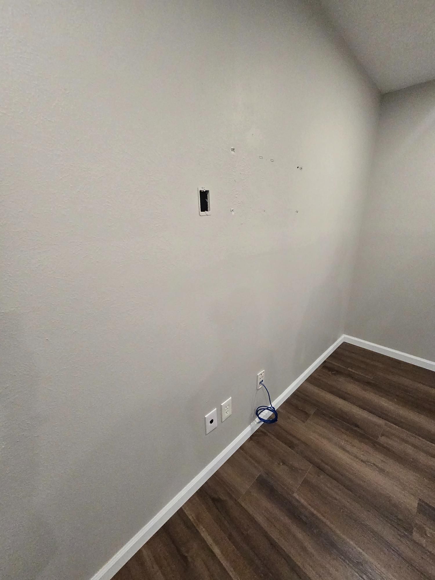 Empty interior wall with a power outlet, cable connection, and flooring.