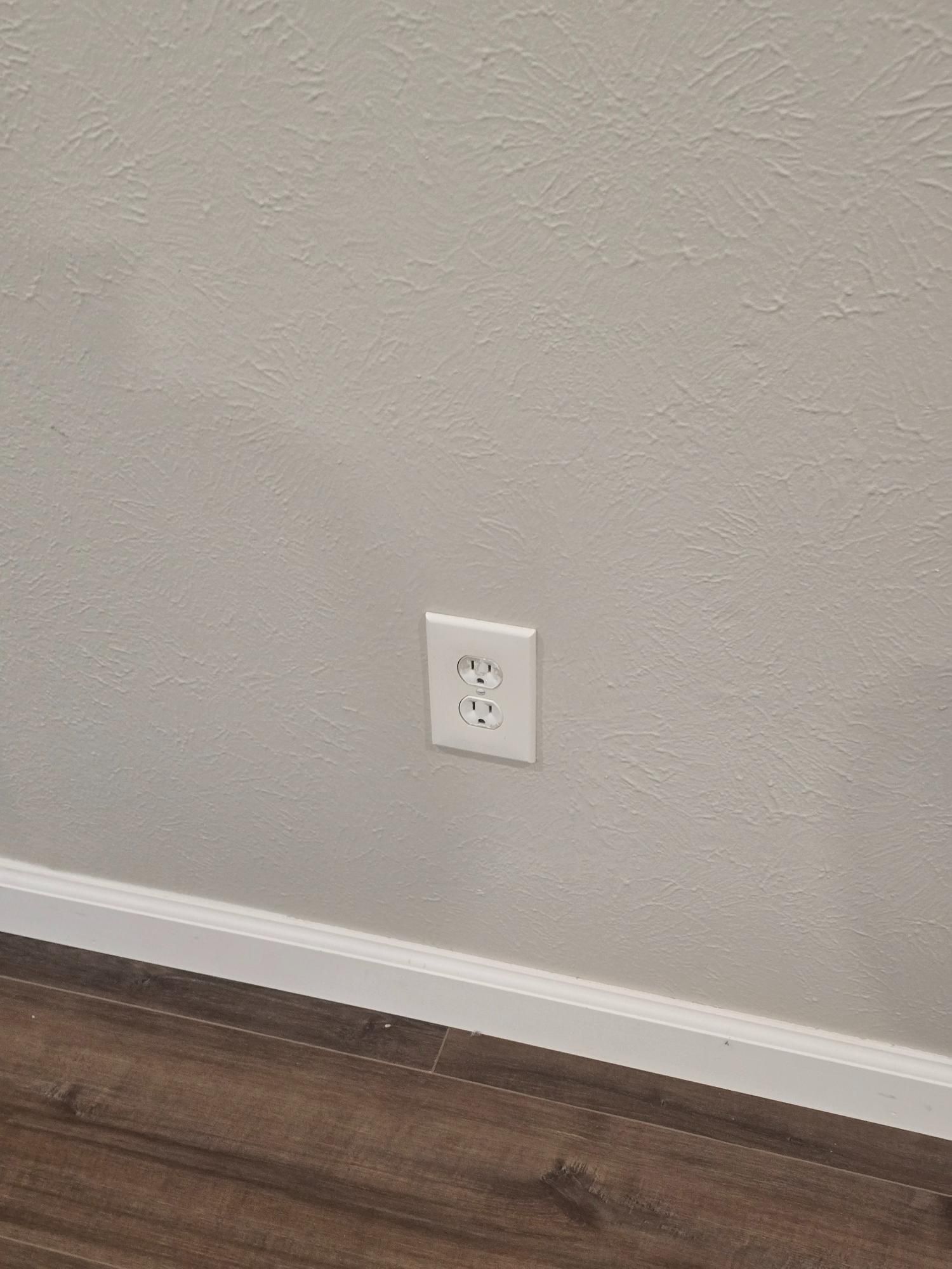 White electrical outlet on a light gray wall above a wooden floor and white baseboard.