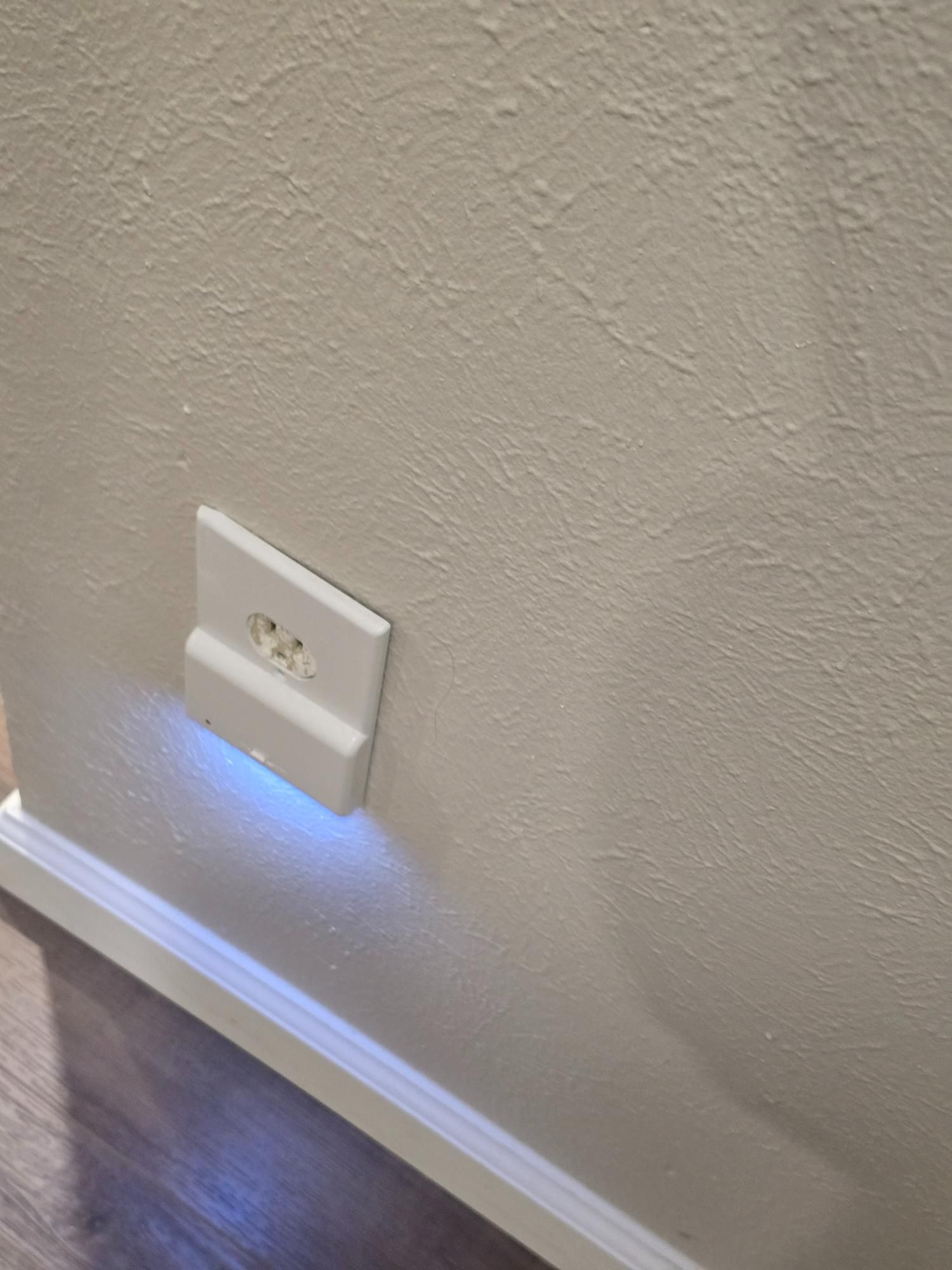 White electrical outlet with built-in blue night light on textured off-white wall.