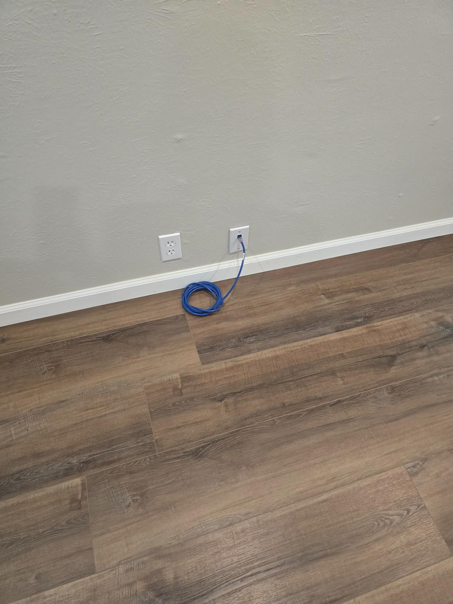 Blue network cable coiled on the floor near two electrical outlets on a gray wall.