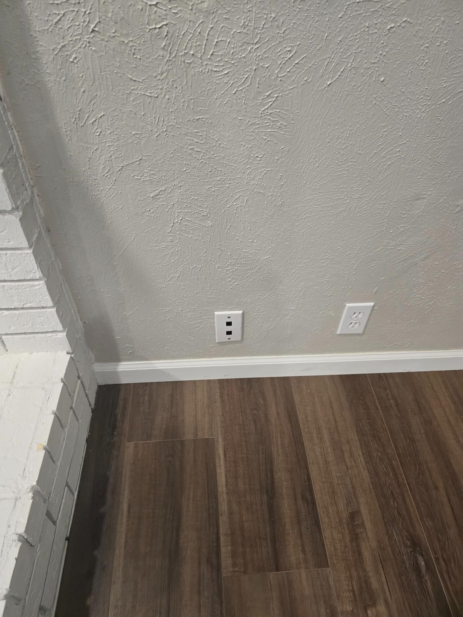 White wall with two outlets, wood-look floor, and brick fireplace.