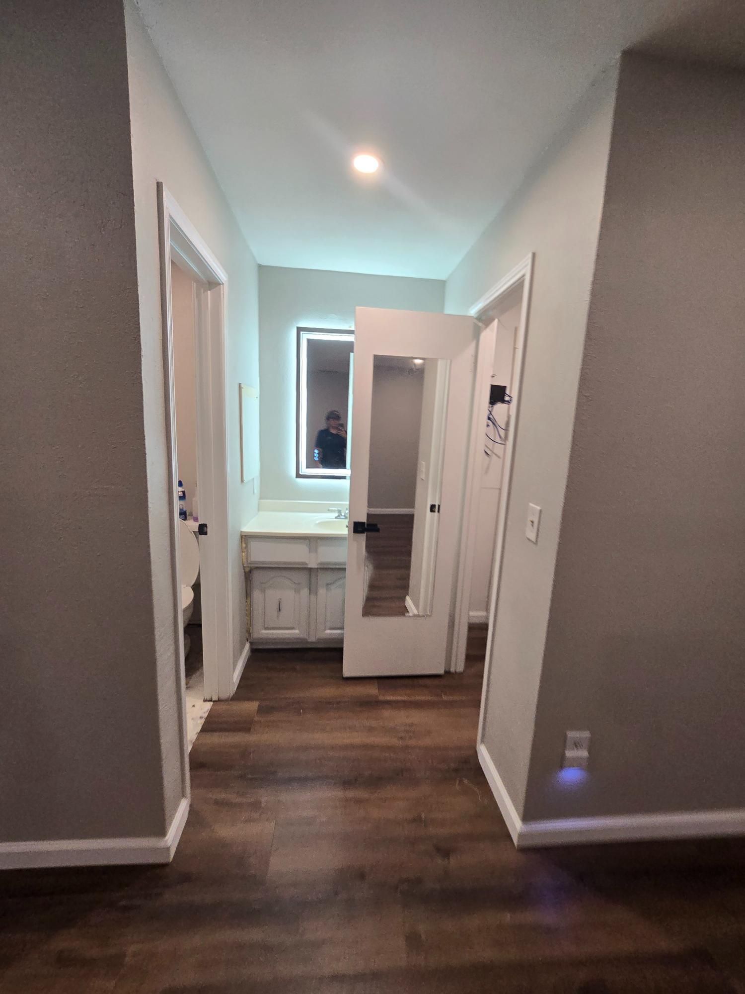 Hallway with wood floor, doors on each side, vanity with a lit mirror at the end.