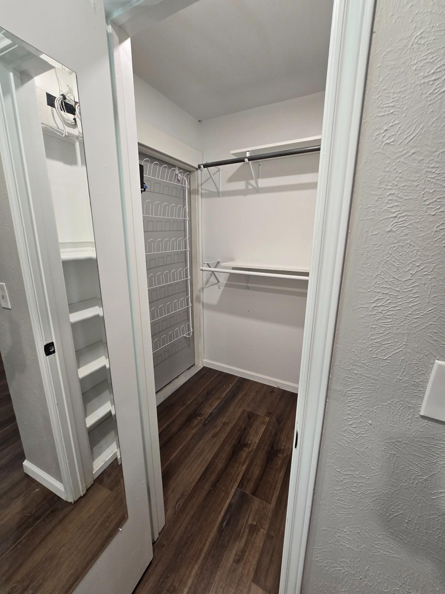 Empty walk-in closet with shelves and clothes rod. Hardwood floor, white trim, grey walls, and sliding door.