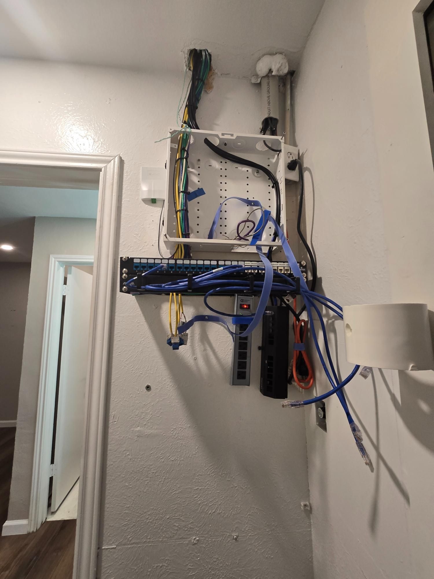Network cables and components mounted on a wall in a home, including a rack, enclosure, and patch panel.