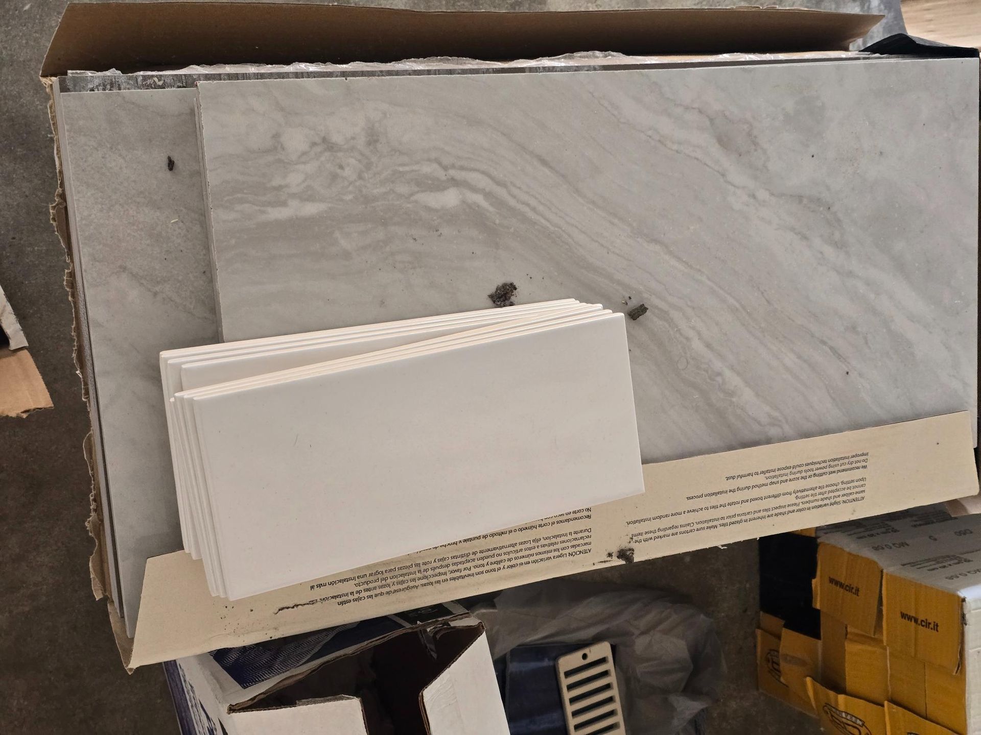 Cardboard box with stacks of gray and white tiles.