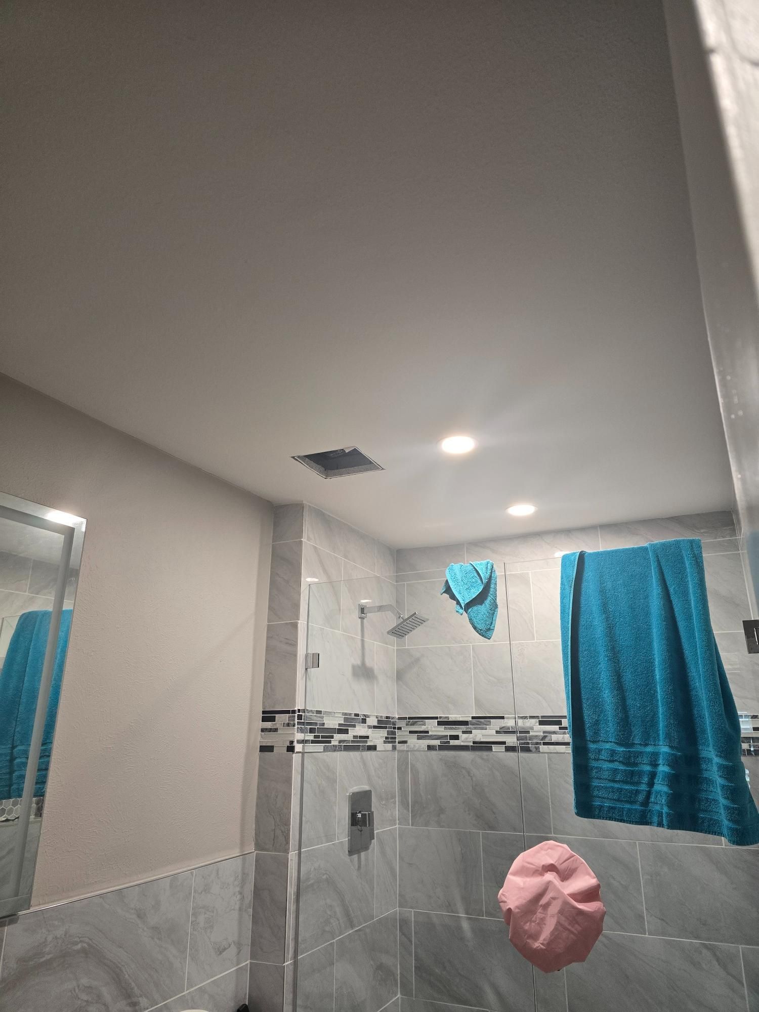 Bathroom with shower, towels, and lights. Blue, gray, and white tile.