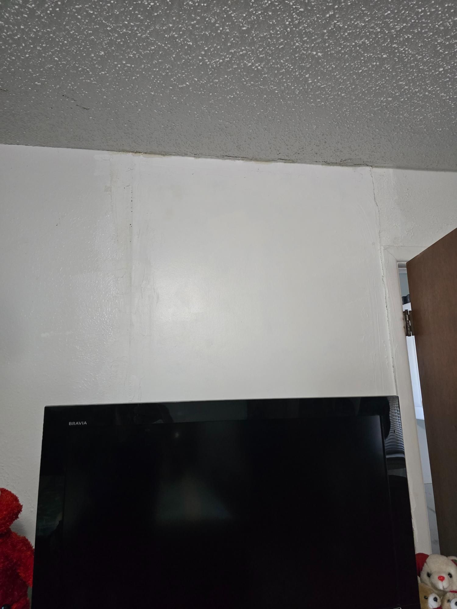 White wall with a black television mounted below a textured ceiling and a doorway.