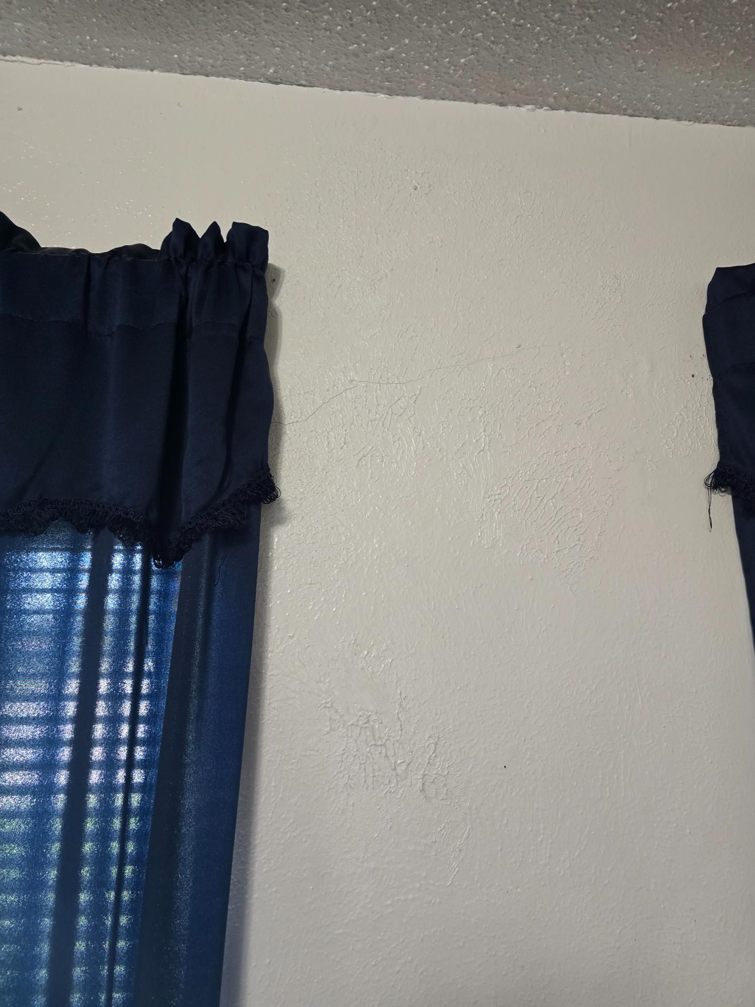 Blue curtains frame a window, beside a white wall and textured ceiling.