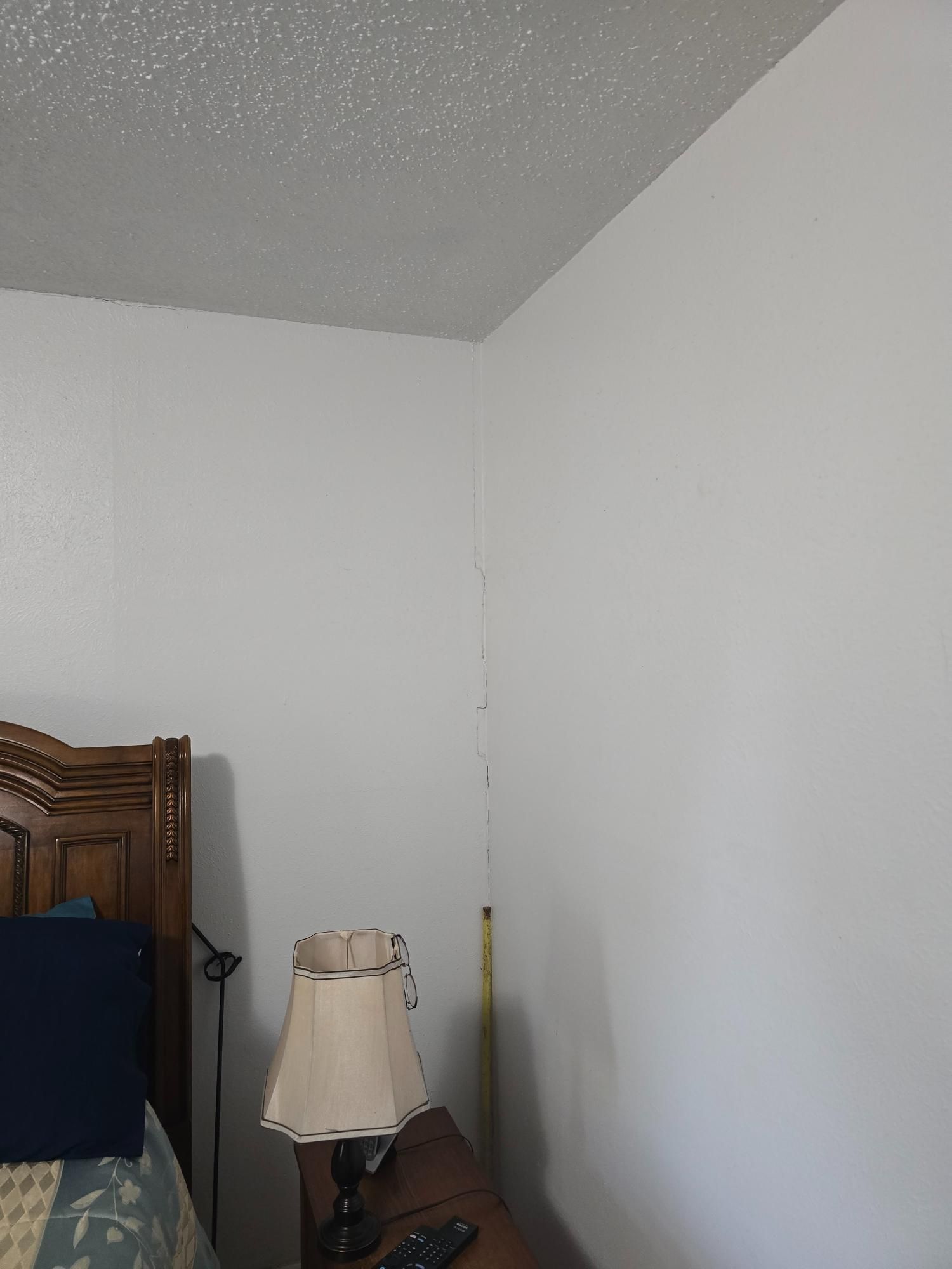 White walls meet a textured ceiling in a corner of a room, next to a bed and lamp.