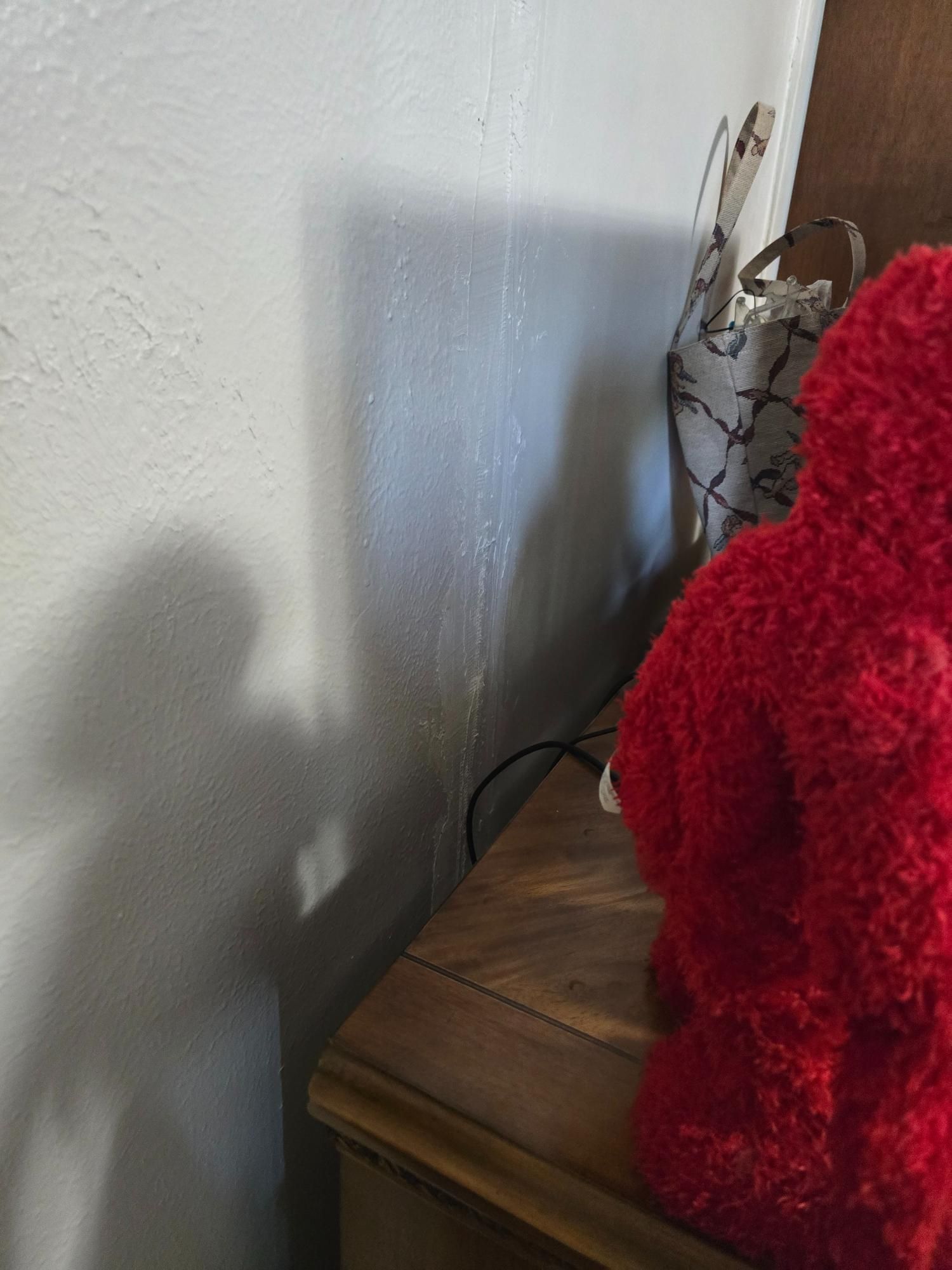 Red plush toy on a wooden dresser next to a white wall with a vertical stain.