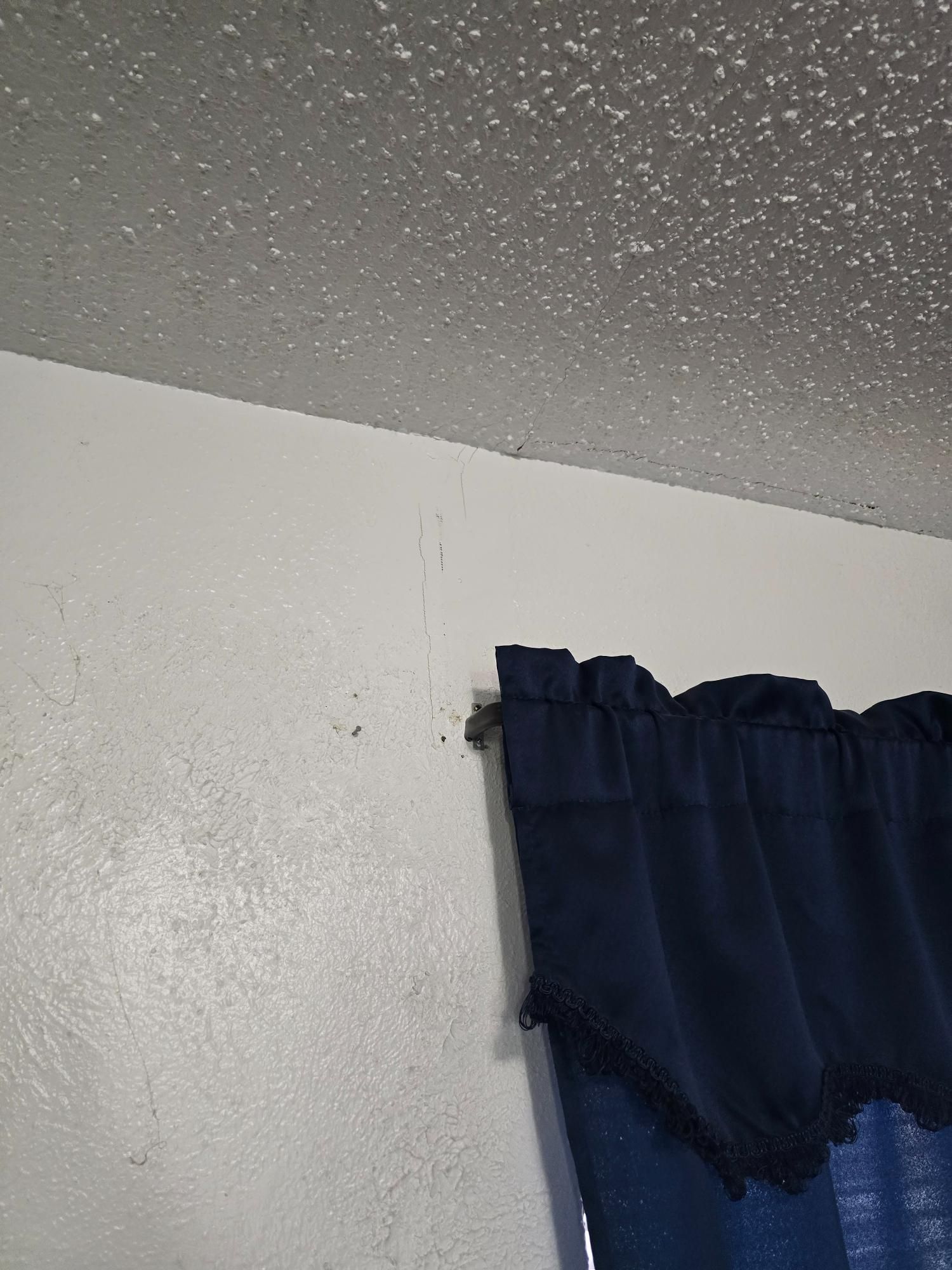 White wall with dark blue curtain next to a textured white ceiling.