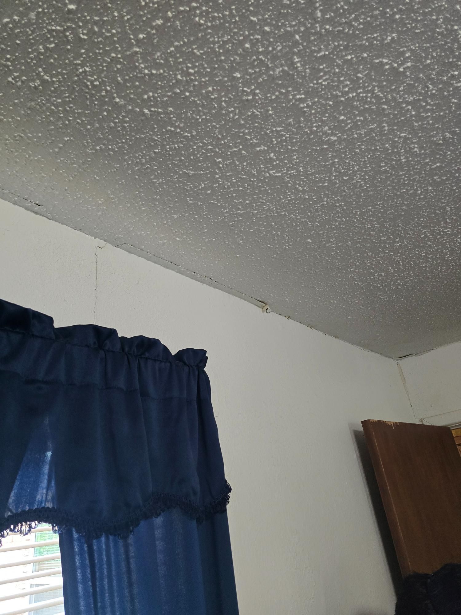 Blue curtain, white walls, and popcorn ceiling in a room.