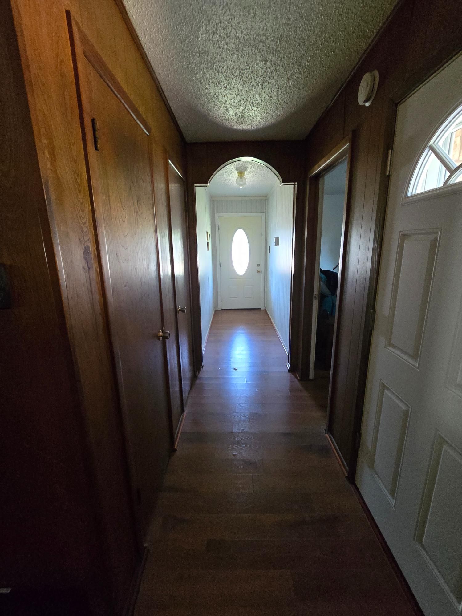 Narrow hallway with wooden walls and flooring, leading to a white door.
