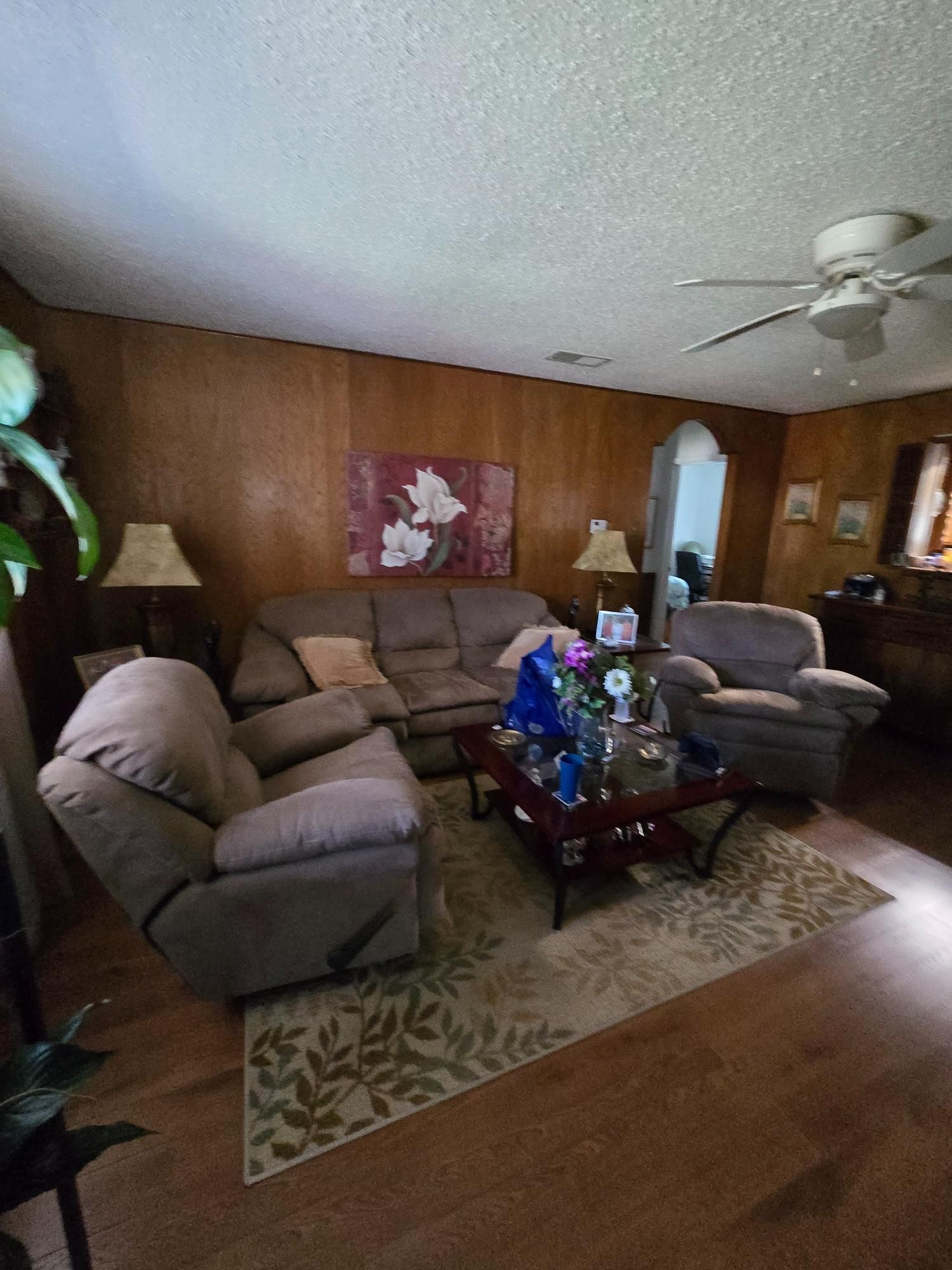 Living room with wooden paneling, beige furniture, floral rug, and ceiling fan.