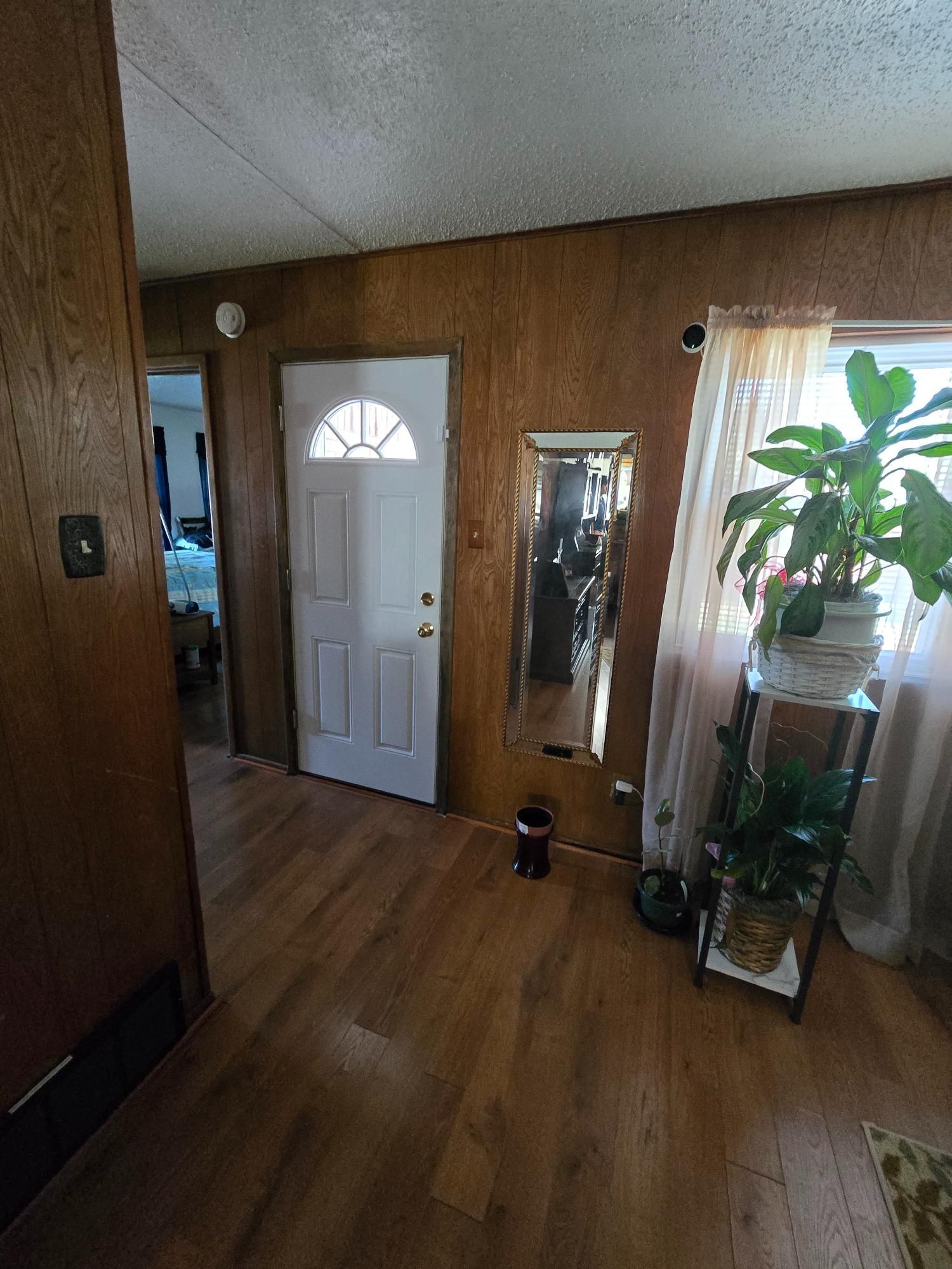 Hallway with white door, mirror, wooden paneling, and a plant stand with plants.