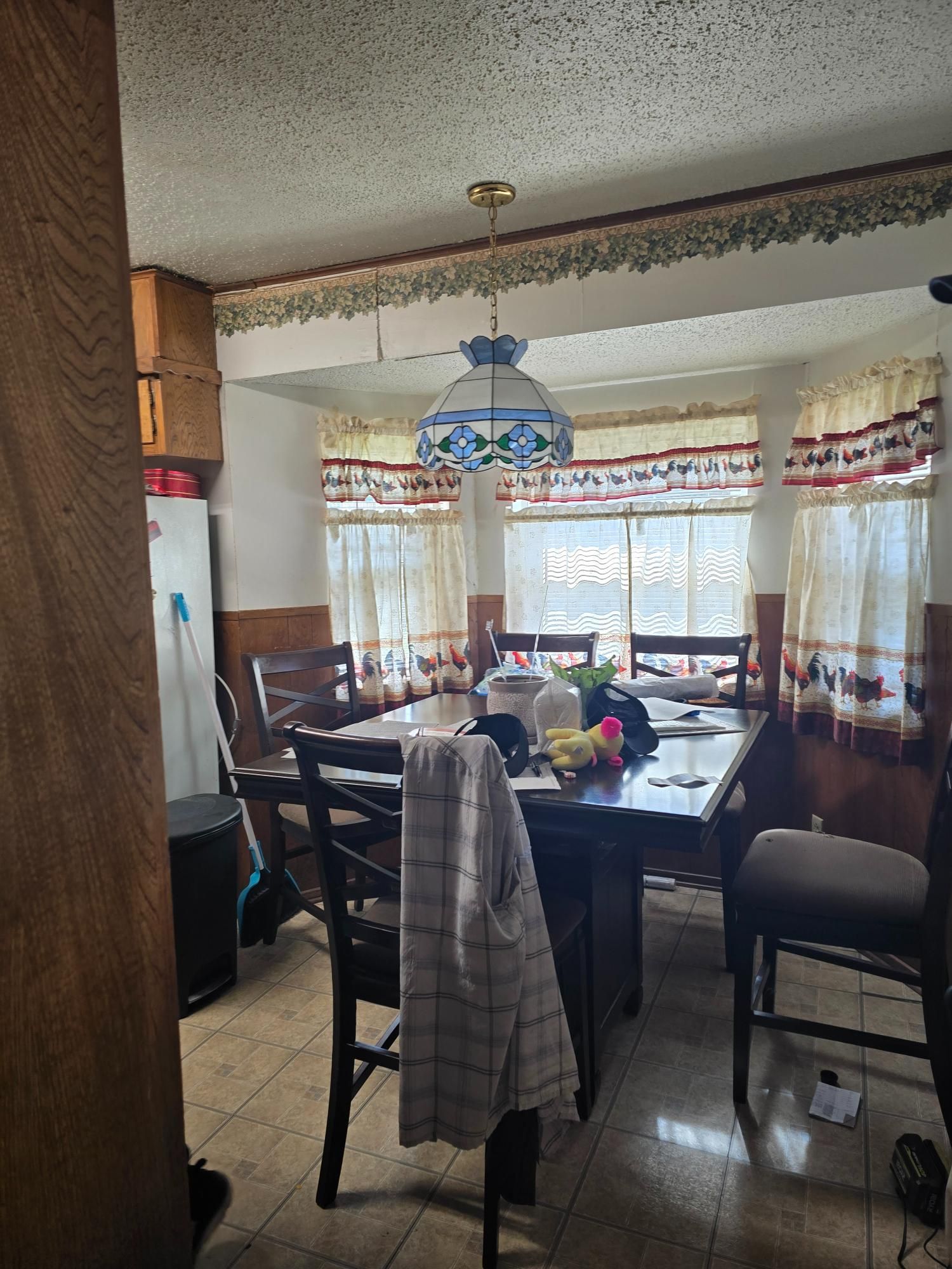 Dining room with dark wooden table and chairs, bay windows with patterned curtains, and a hanging light.