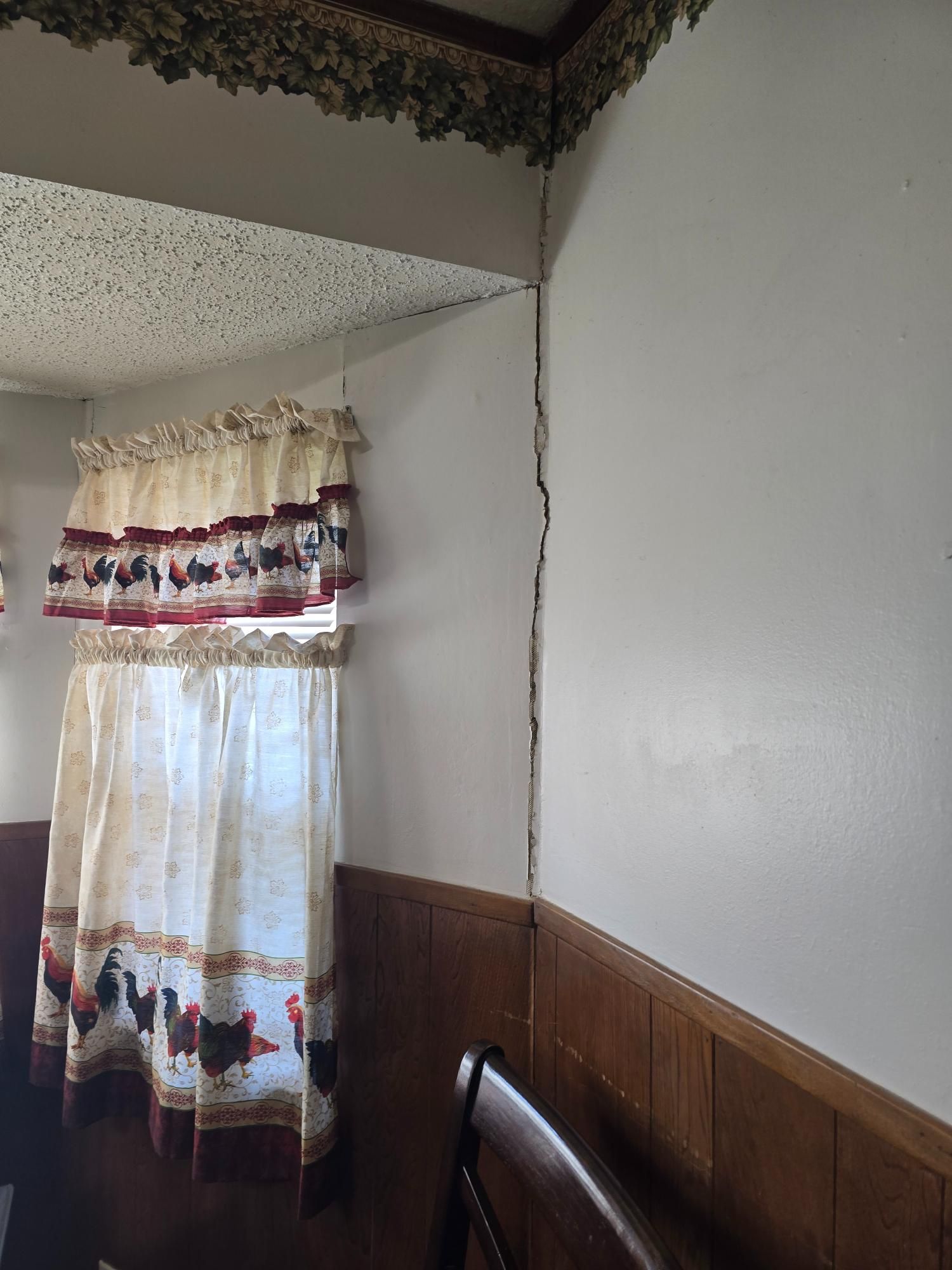 Interior wall with a large vertical crack. A window with a curtain is on the left.