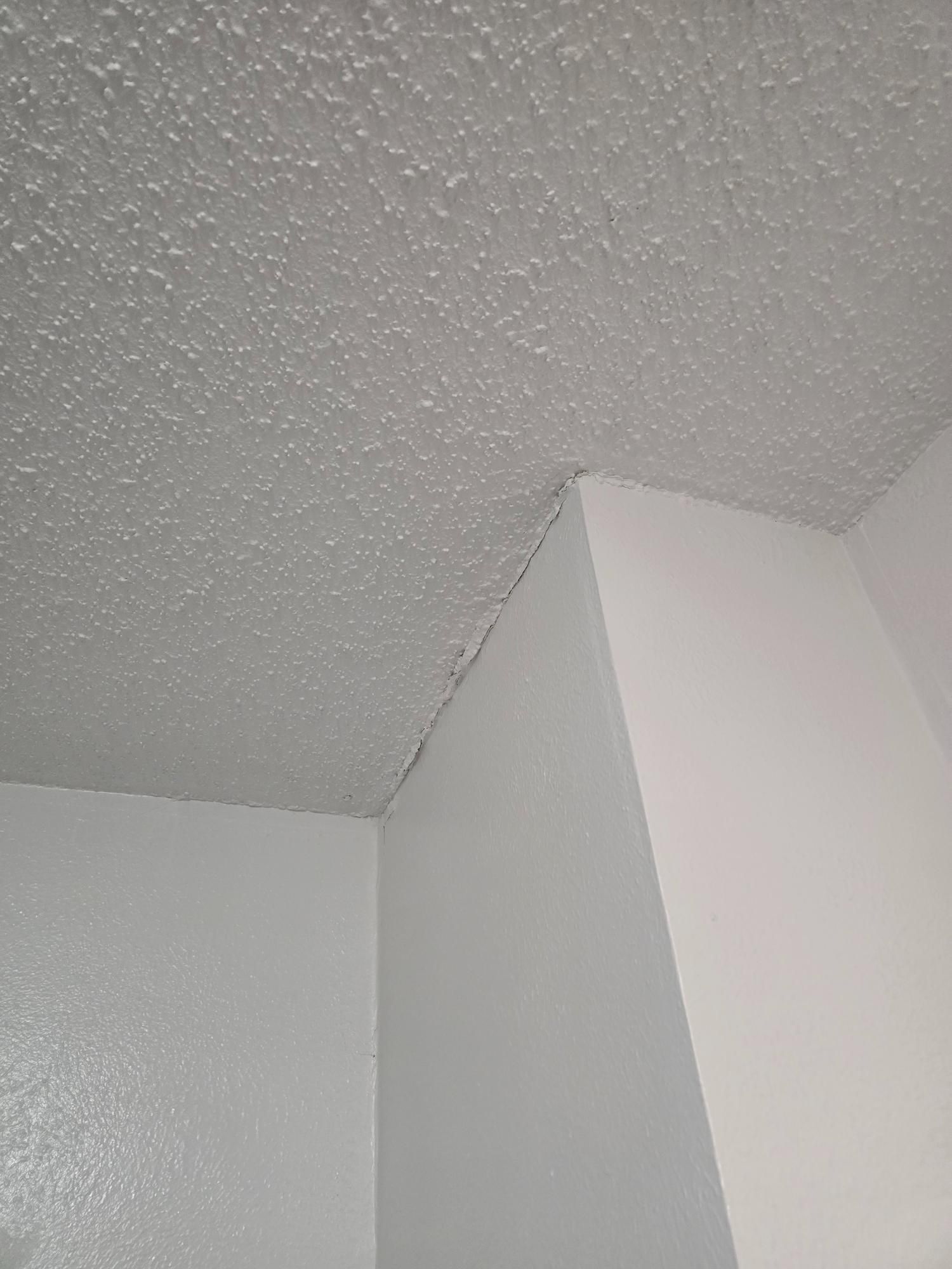 White ceiling with popcorn texture meeting white walls at a corner, showing a crack along the seam.