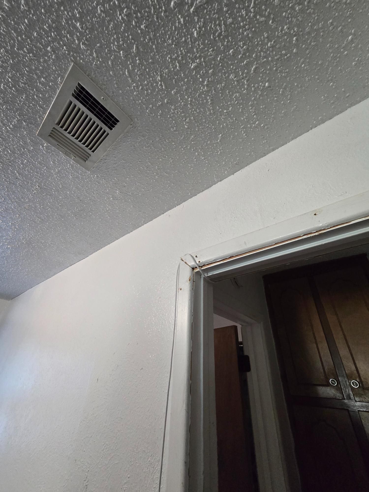 White ceiling with a vent and white door frame with dark cabinets visible.