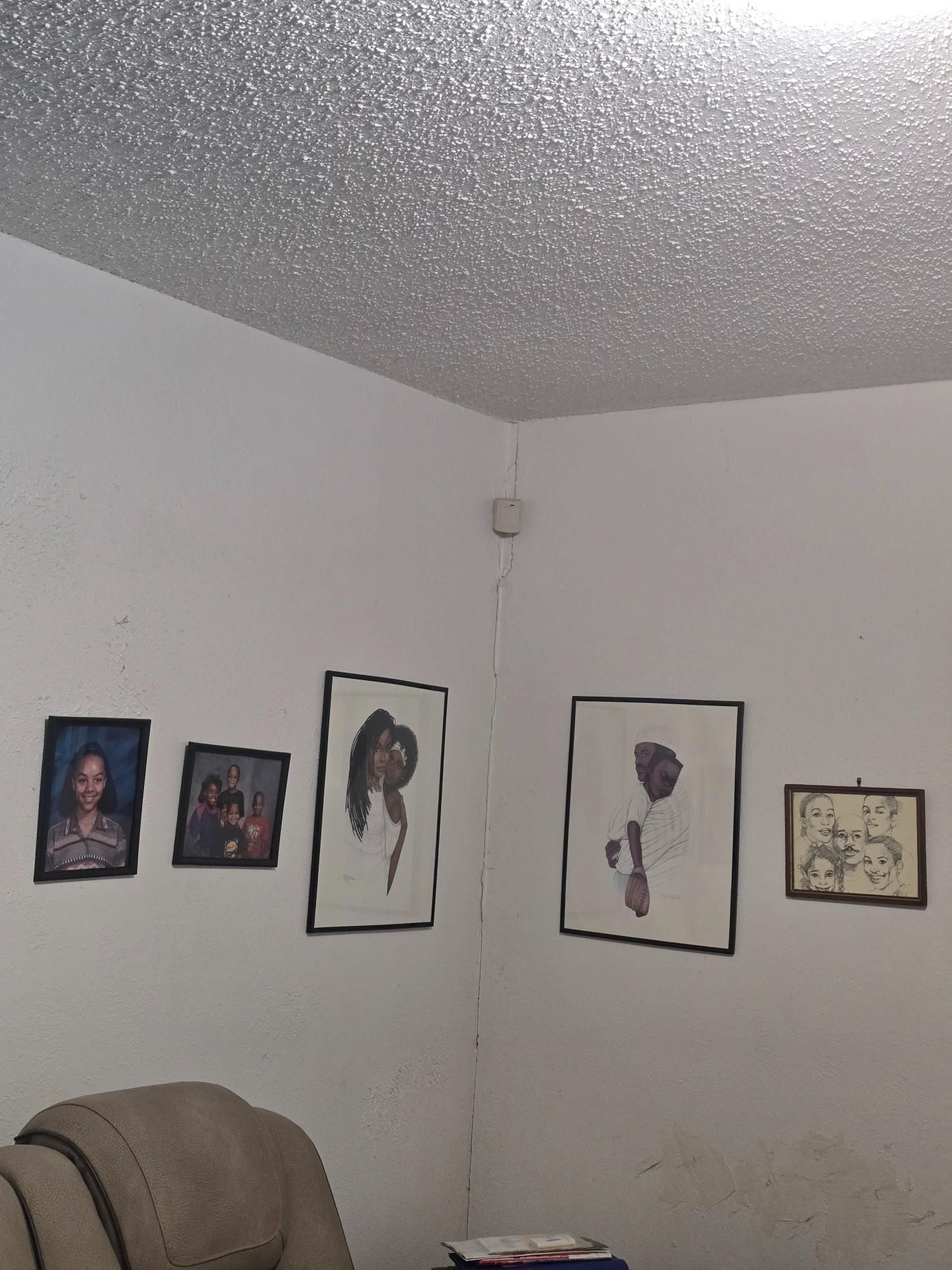Corner of a room with portraits on white walls, popcorn ceiling, and a recliner.