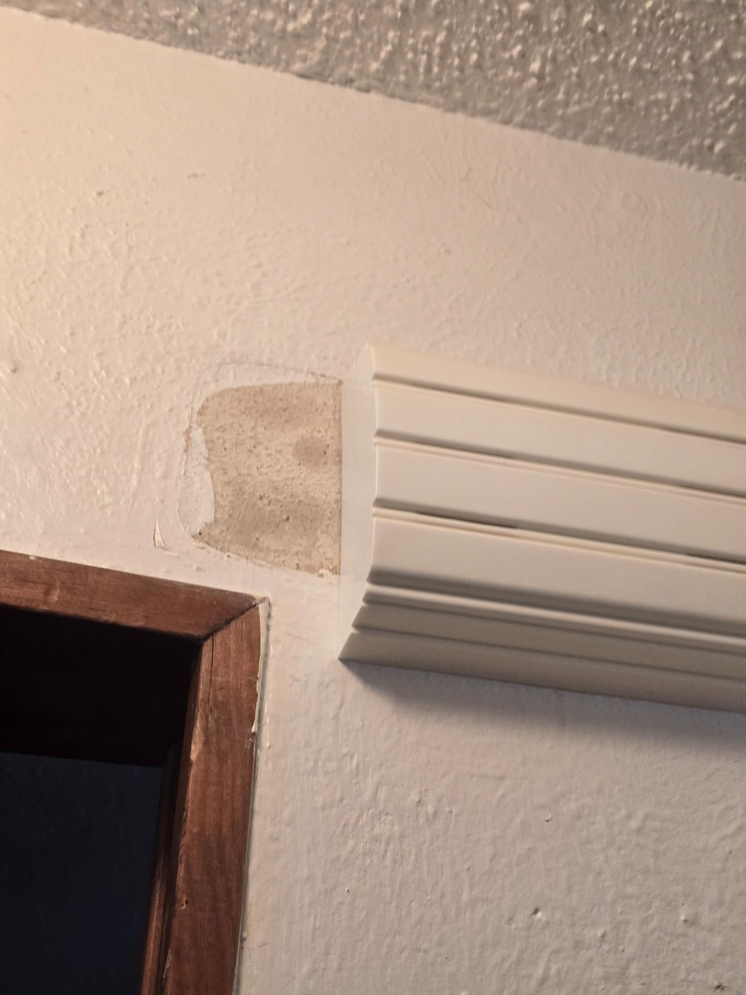 Wall with peeling paint, adjacent to white molding and a wooden door frame.