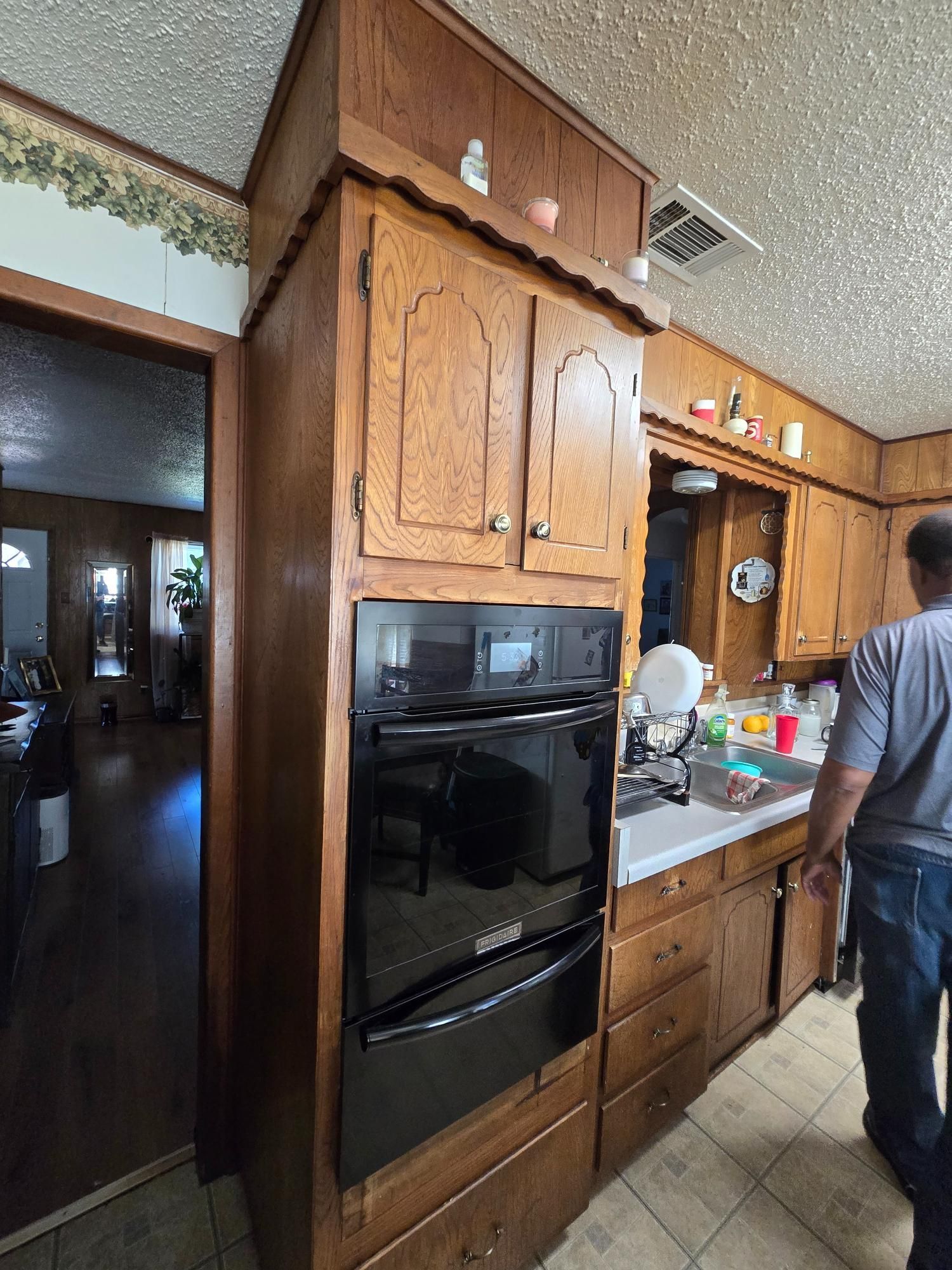 Kitchen with dark wood cabinets, a black oven, and a person standing next to the counter.