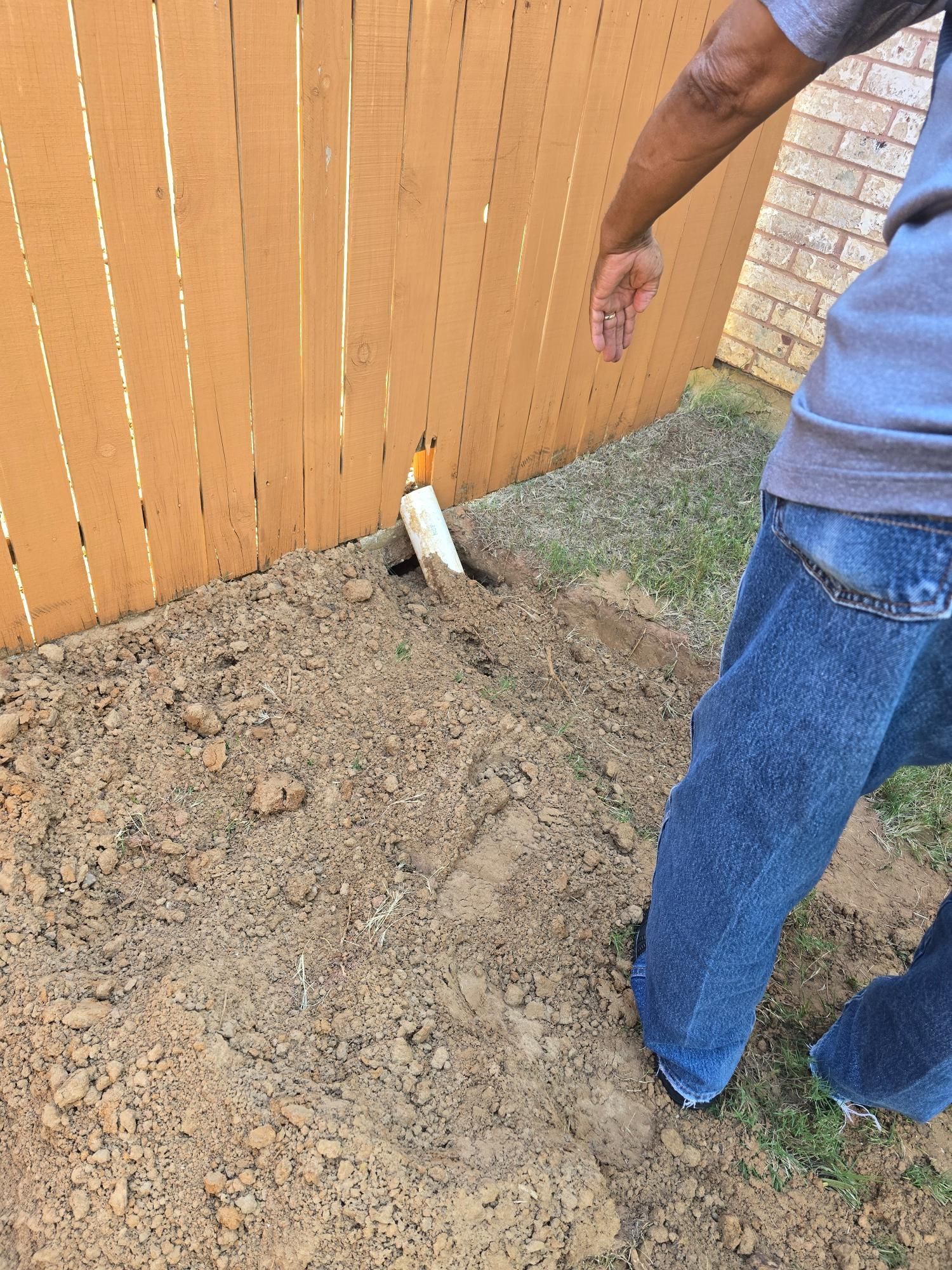 A person next to a partially buried white pipe near a wooden fence and dirt.