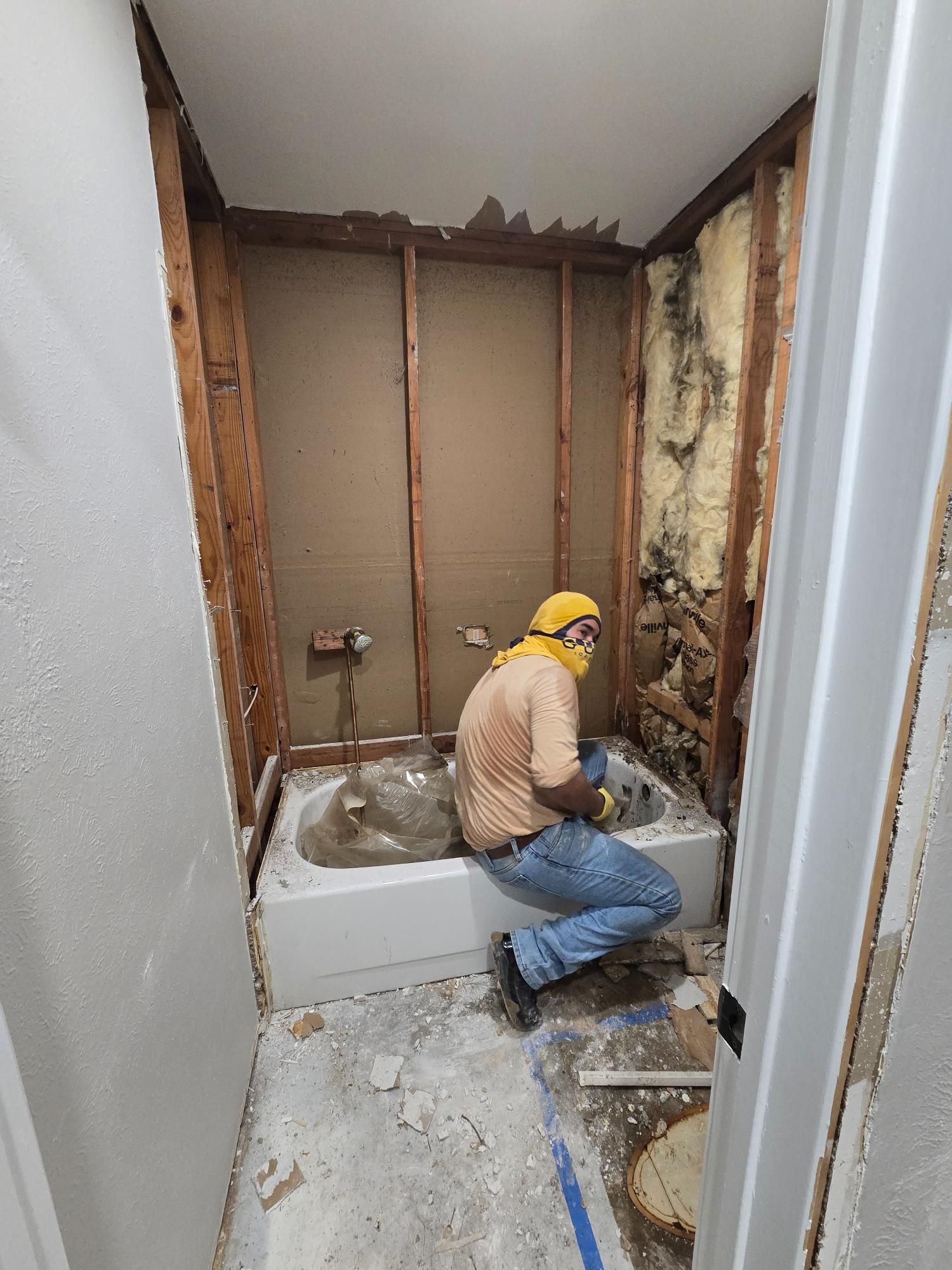A person removes an old bathtub in a bathroom during renovation. The walls are exposed studs.