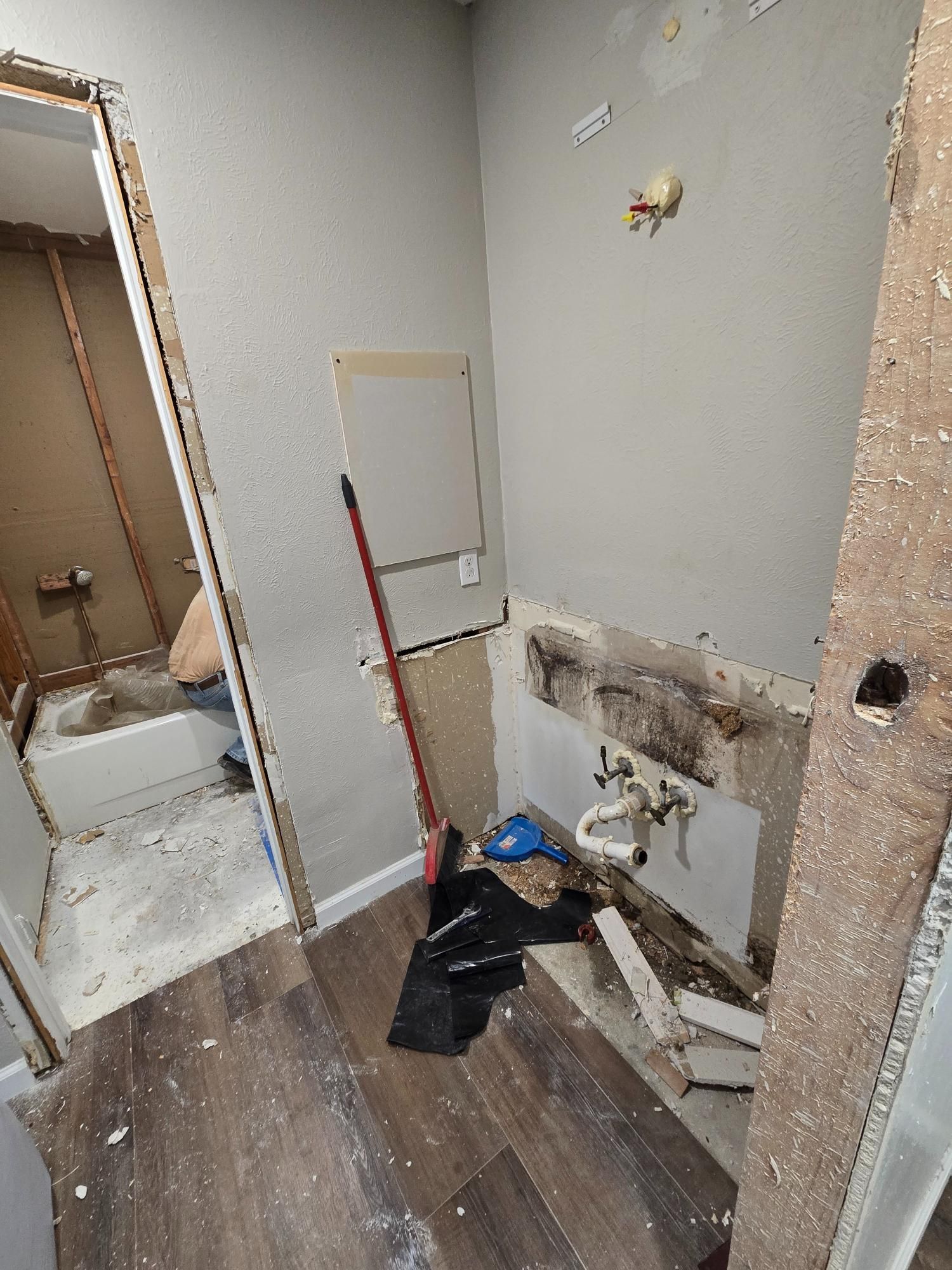 Bathroom renovation in progress; exposed wall, plumbing, and debris. Entryway to tub/shower visible.
