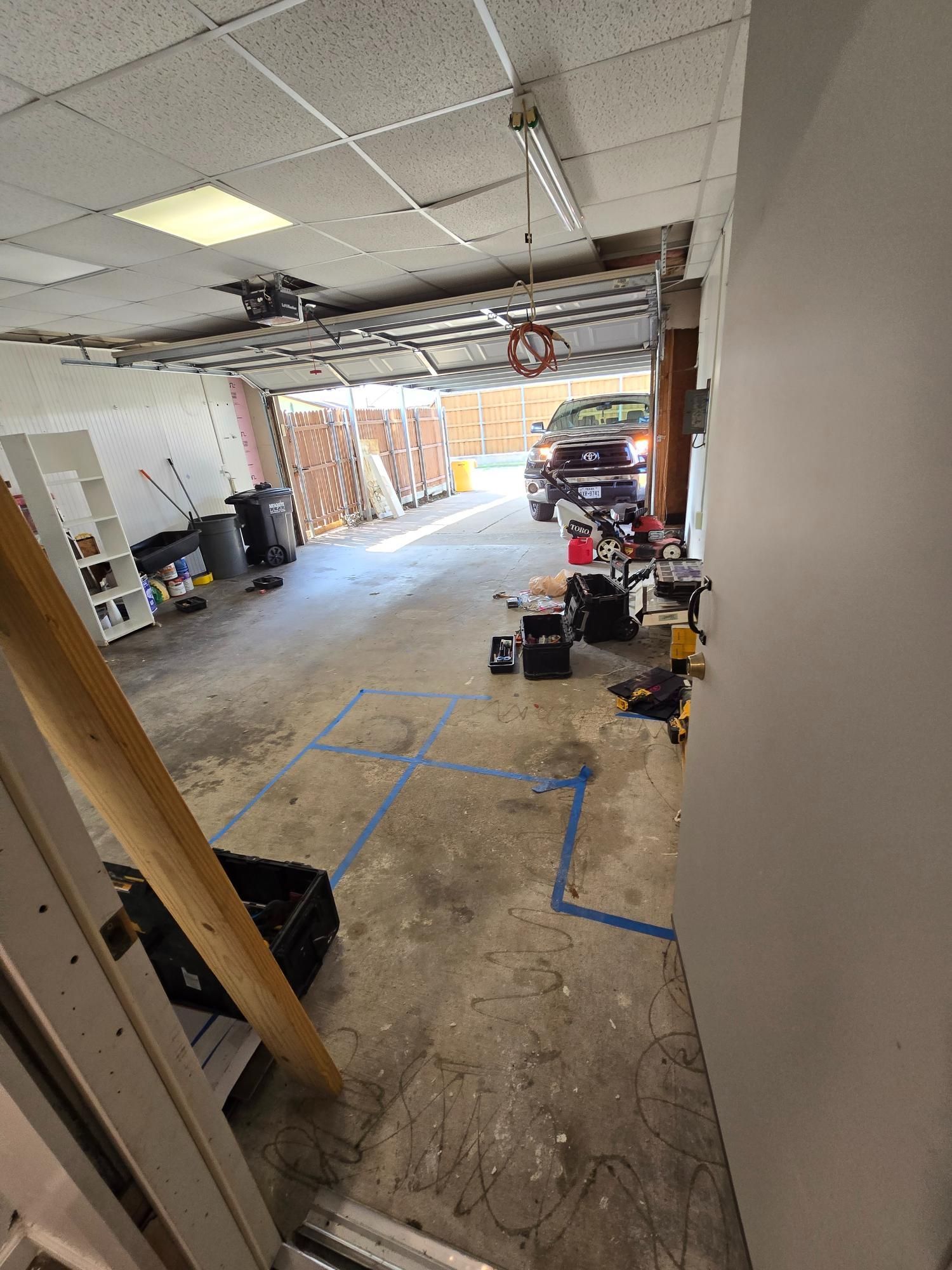 Garage interior with a car parked inside. Tools and debris scattered on the floor. Open garage door.