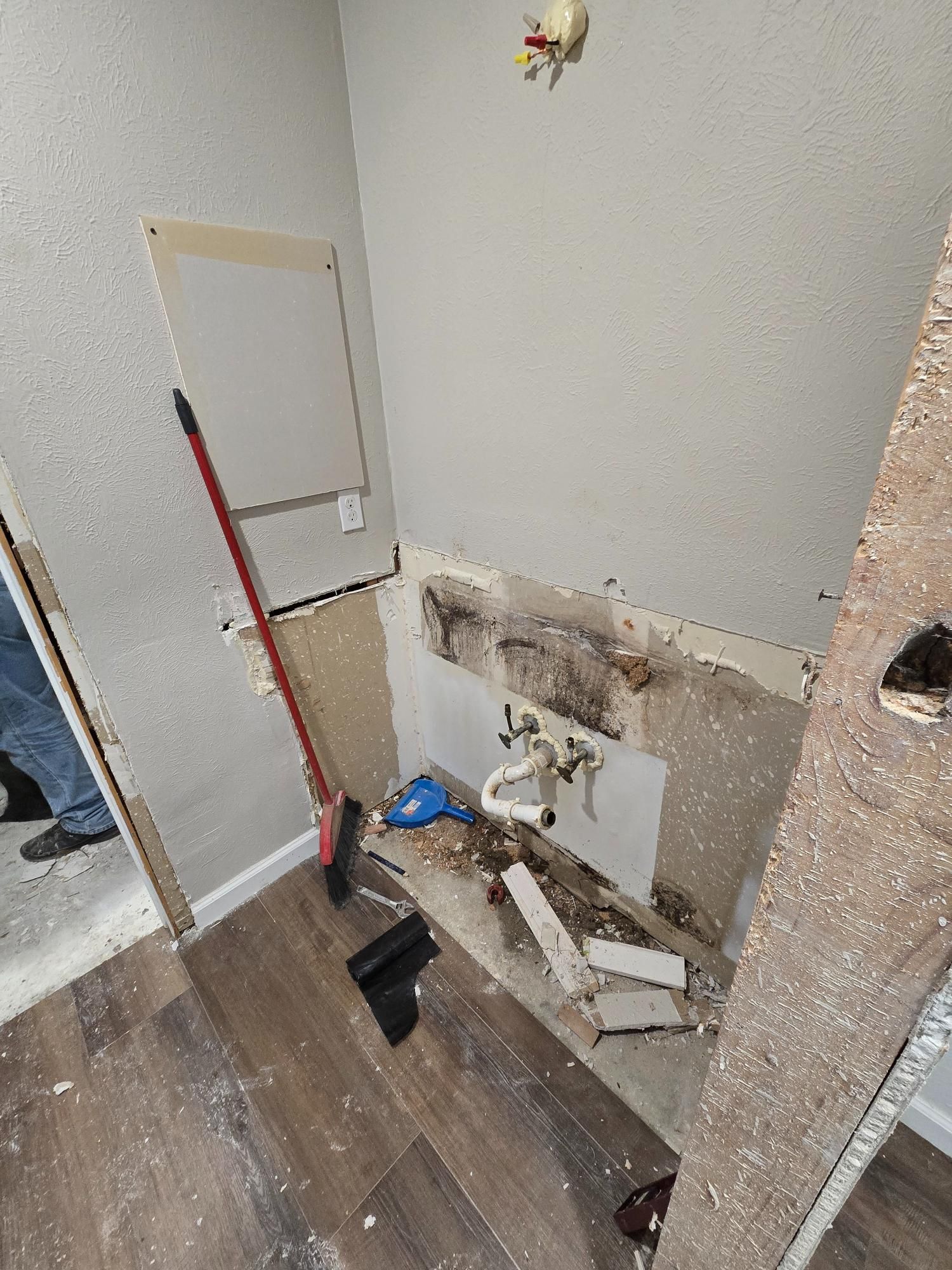 Bathroom demolition in progress: exposed plumbing, damaged wall, debris on floor.
