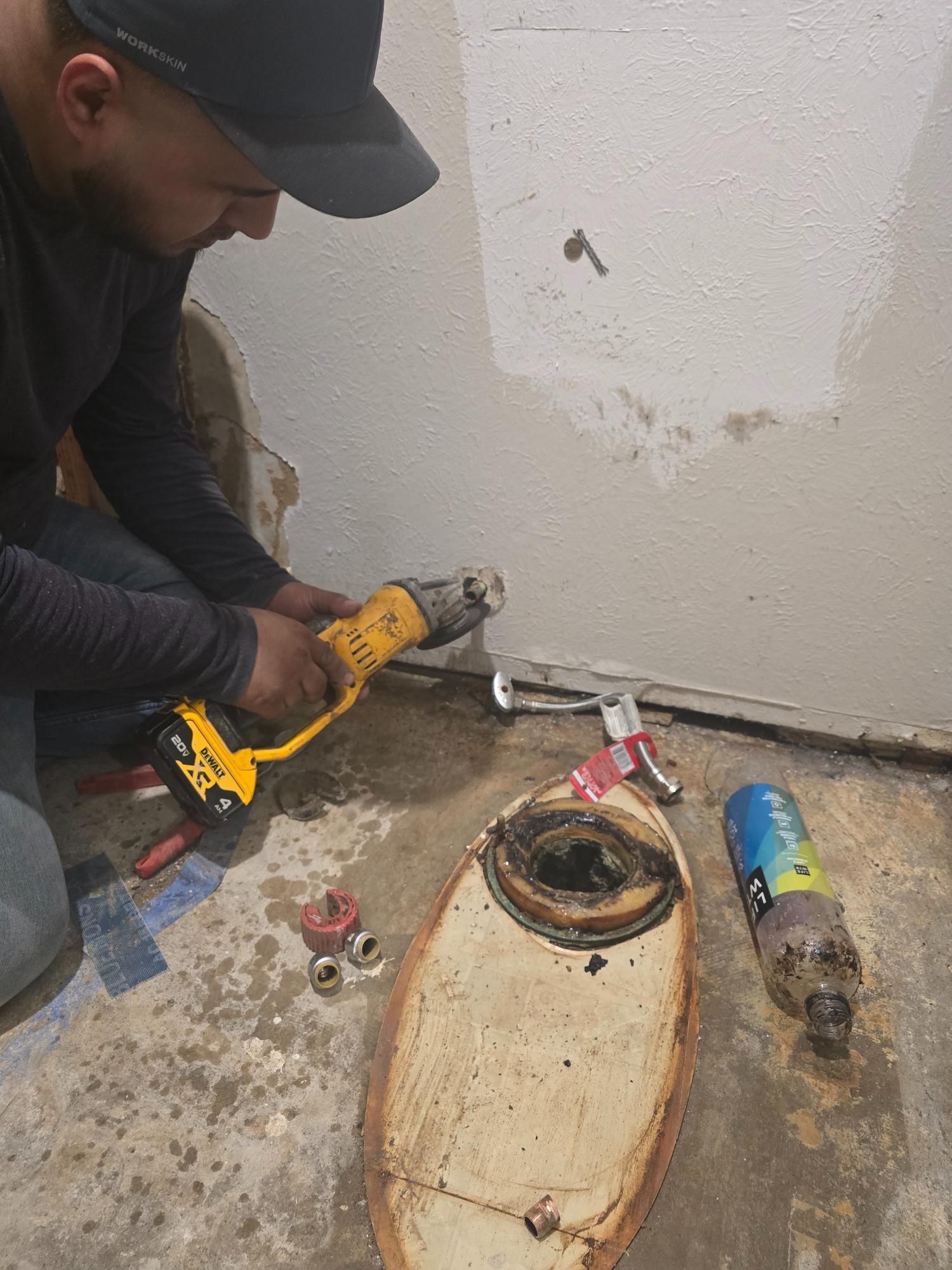 Man using a power tool on a pipe near a wall, next to plumbing fixtures in a work area.