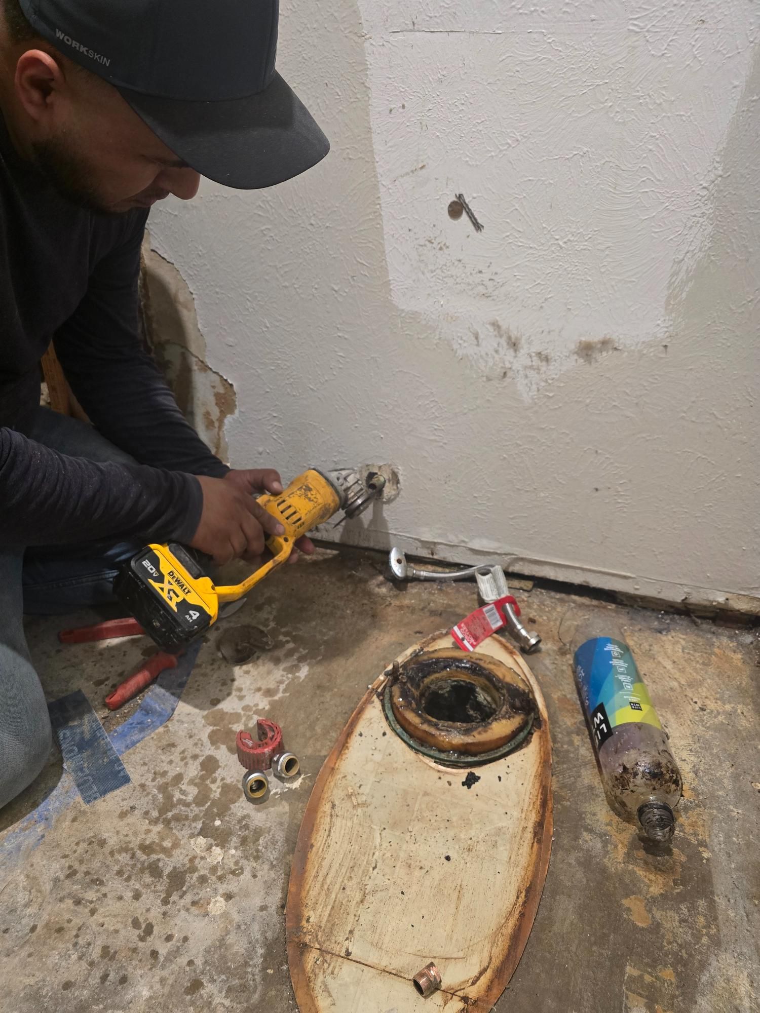 Person cutting a pipe near a wall with tools and a cut fixture on the floor in a work setting.