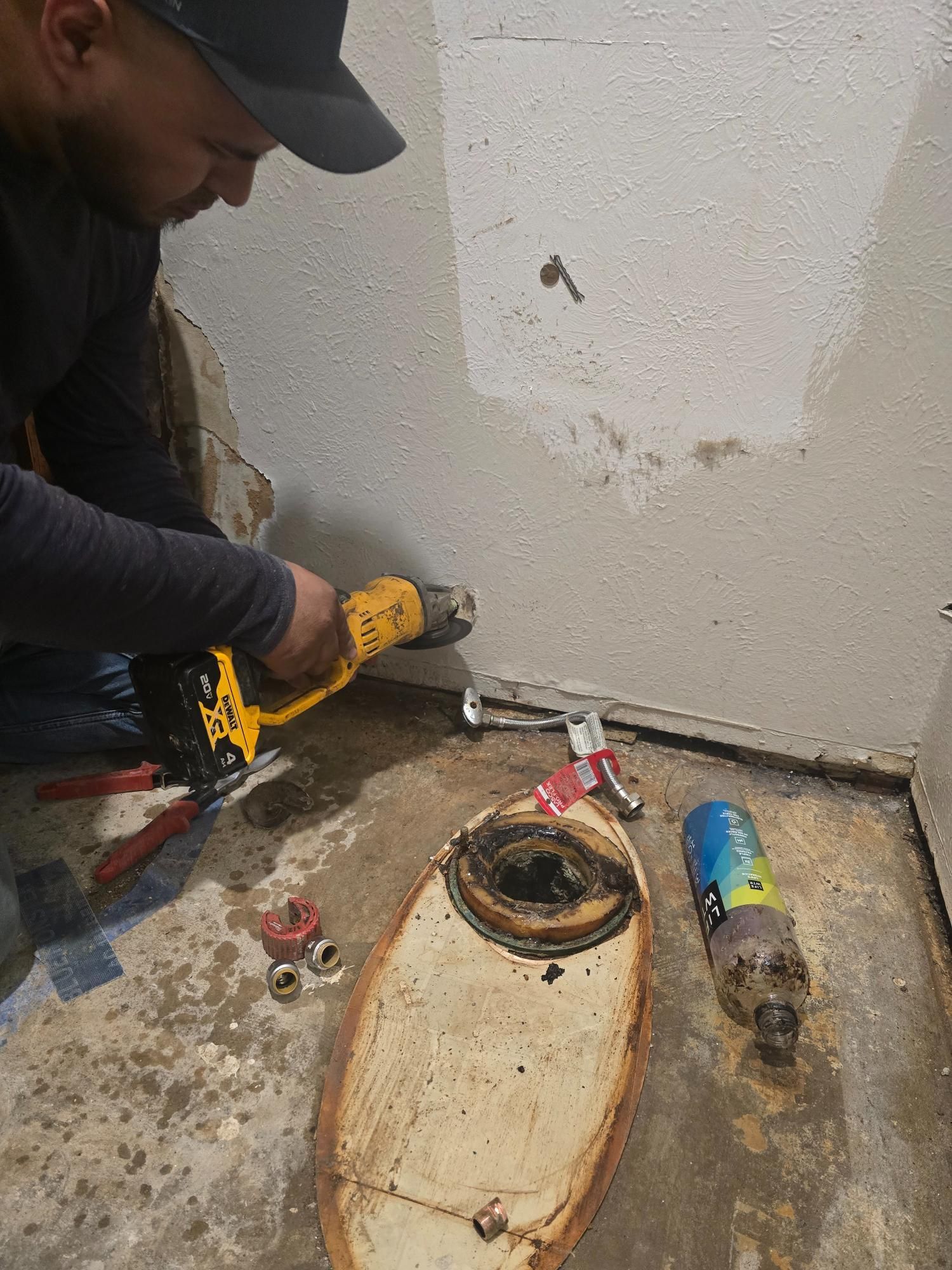 Plumber working on a toilet, using a heat gun. Tools and parts are scattered on a concrete floor.