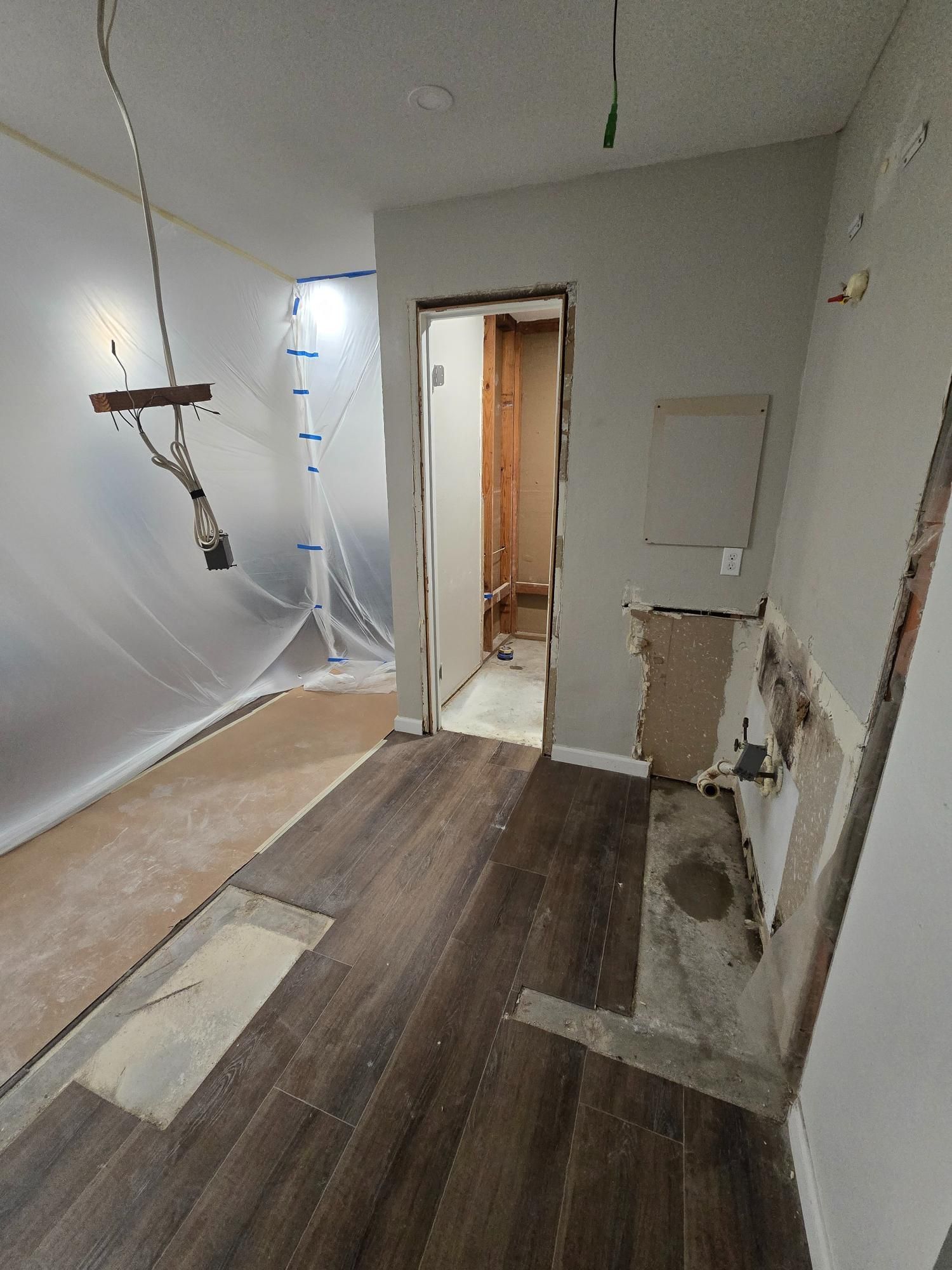 Bathroom renovation with exposed walls, new flooring, and doorway to a toilet area.